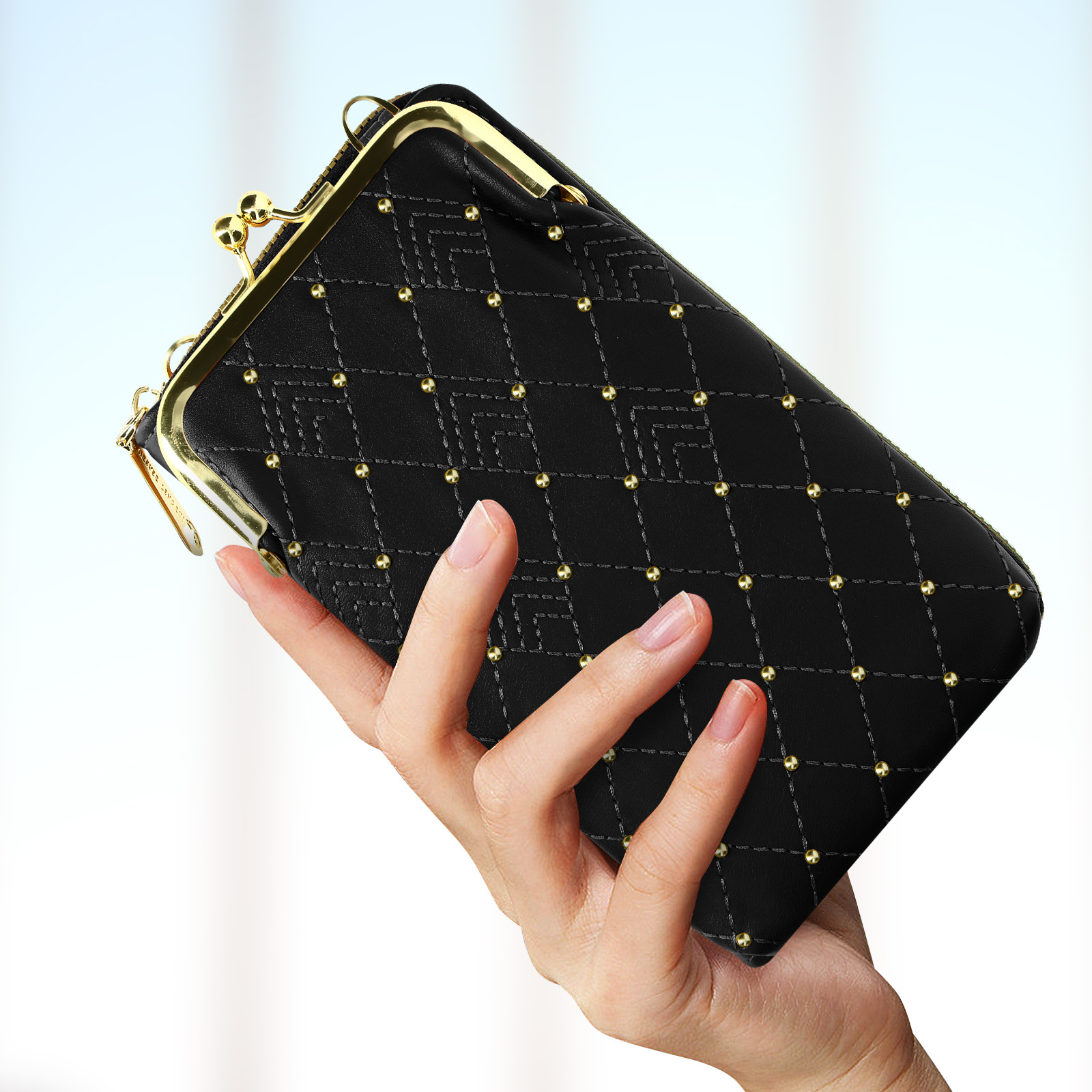 Una pochette nera con dettagli dorati e chiusura, tenuta in mano. È trapuntata con borchie dorate.