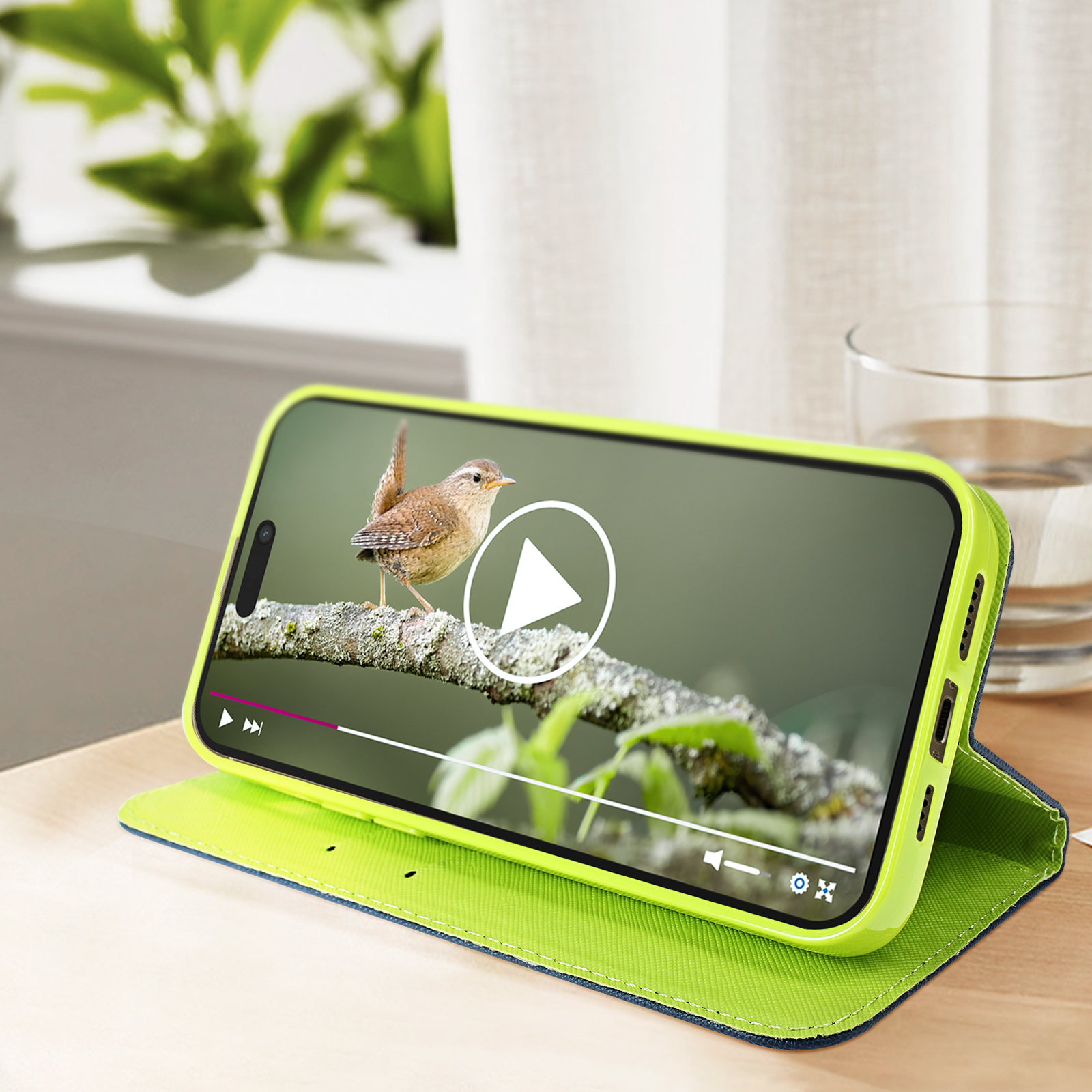 Telefono in custodia verde riproduce un video di un uccello. La custodia è su un tavolo.