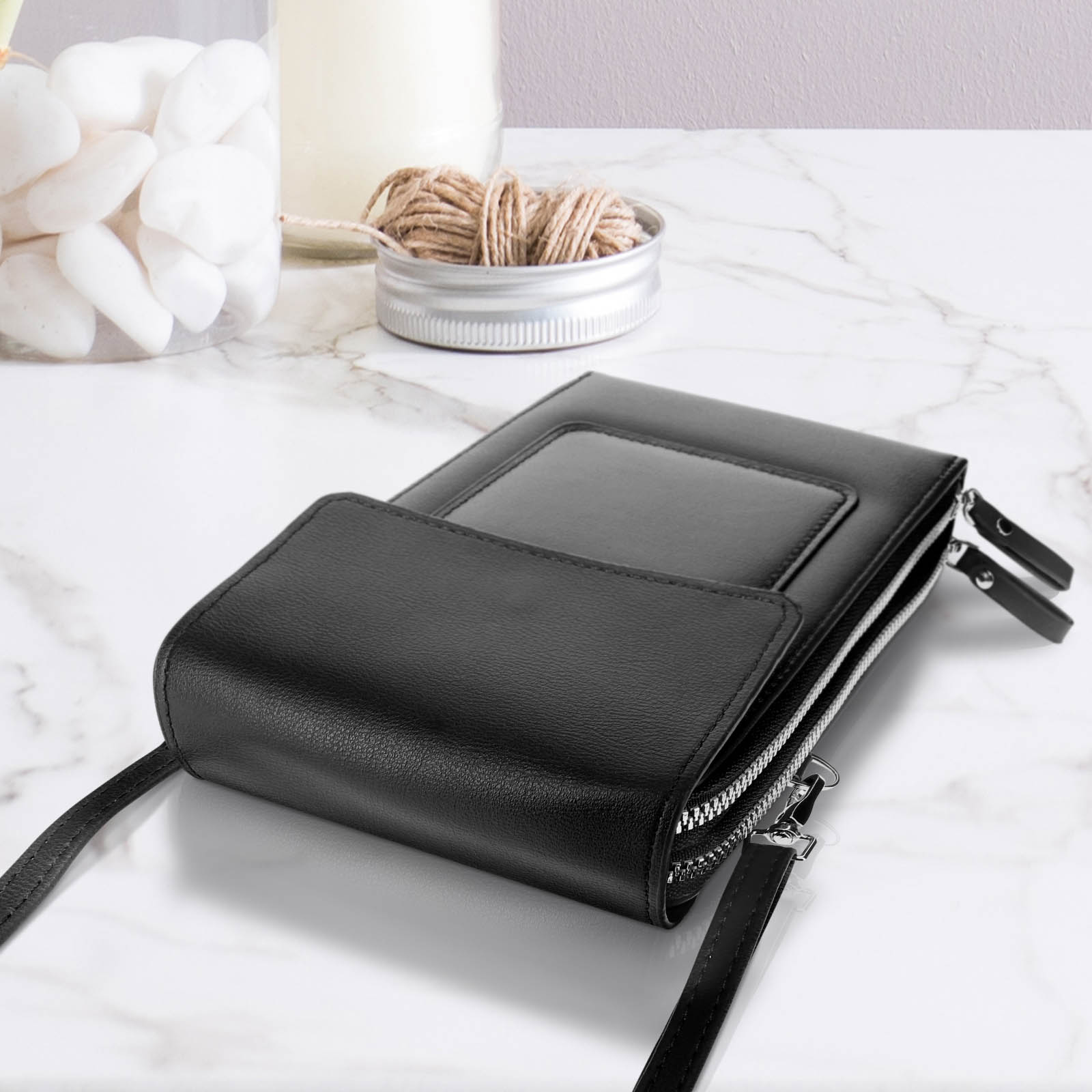 Eine schwarze Telefontasche liegt offen auf einer Marmoroberfläche, mit einem Glas und Schnur.