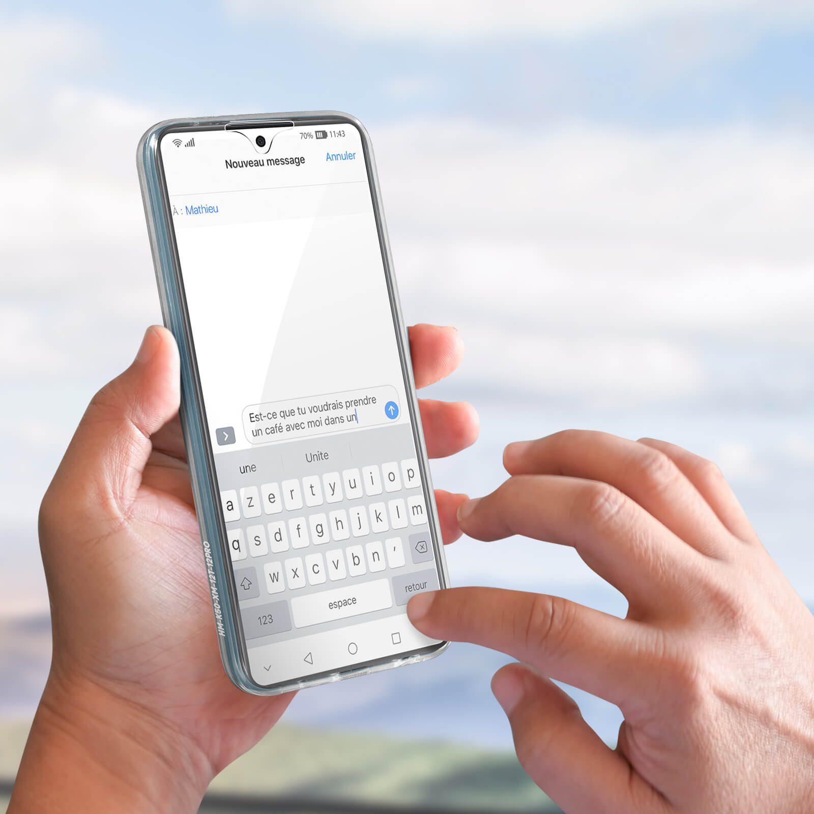 Un telefono con un messaggio di testo in francese viene tenuto in mano. Lo sfondo è un cielo blu.