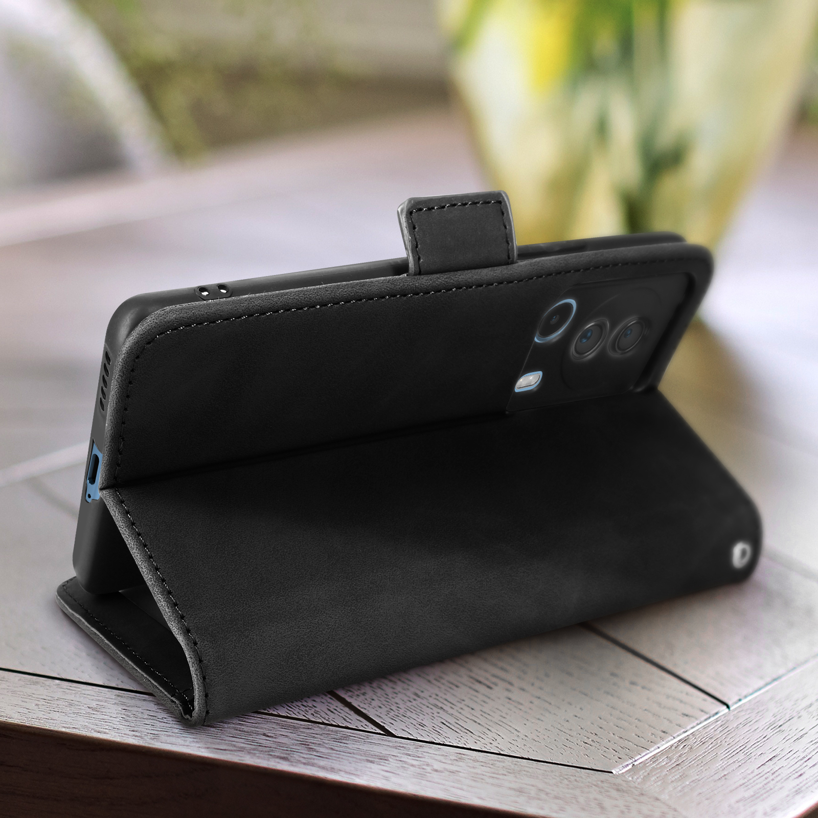 Un telefono nero in una custodia a portafoglio in pelle è aperto. Il telefono ha una fotocamera. La custodia è su una superficie di legno.