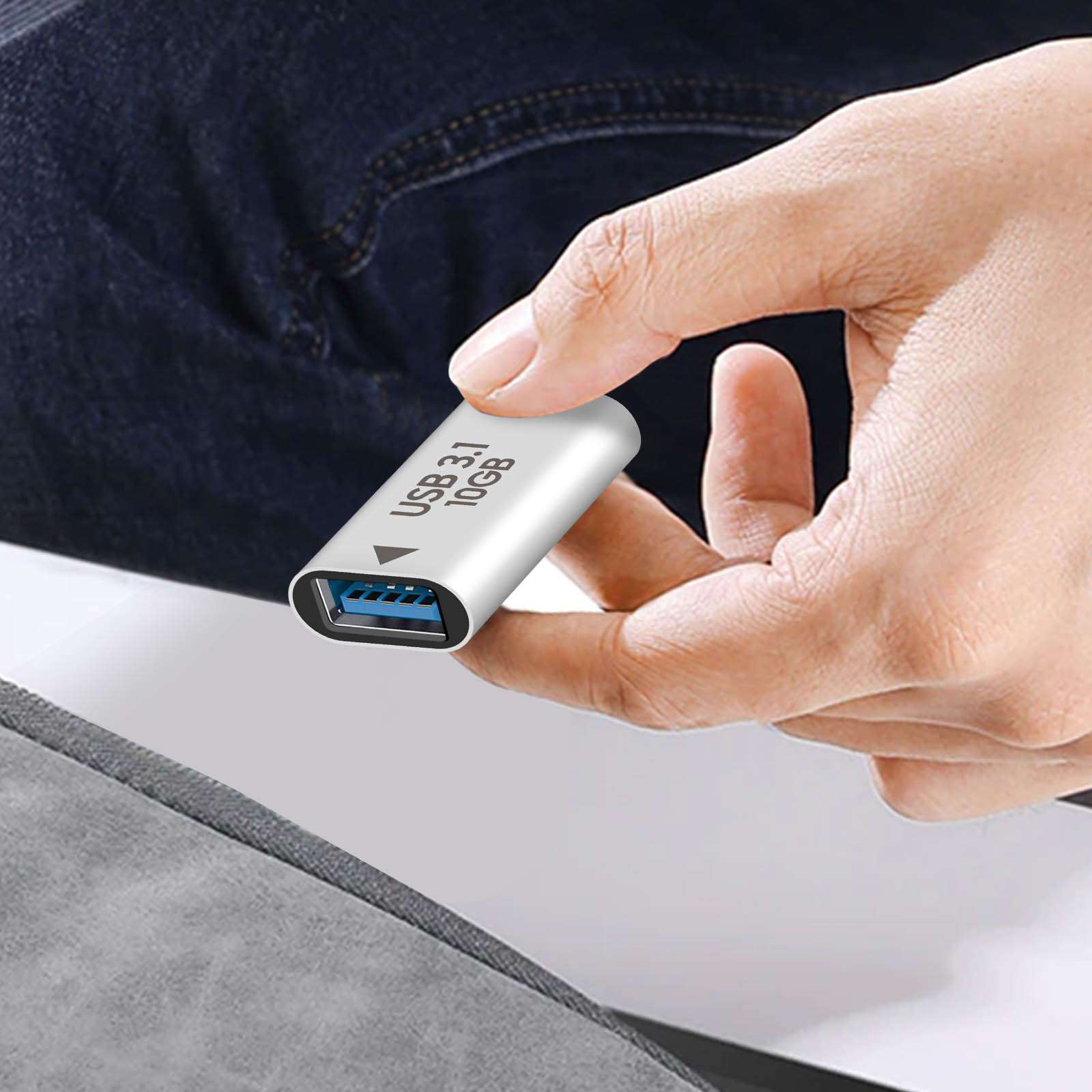 Una mano che tiene una chiavetta USB argentata con la scritta 'USB 3.1 10GB'. L'unità è sopra una superficie grigia.