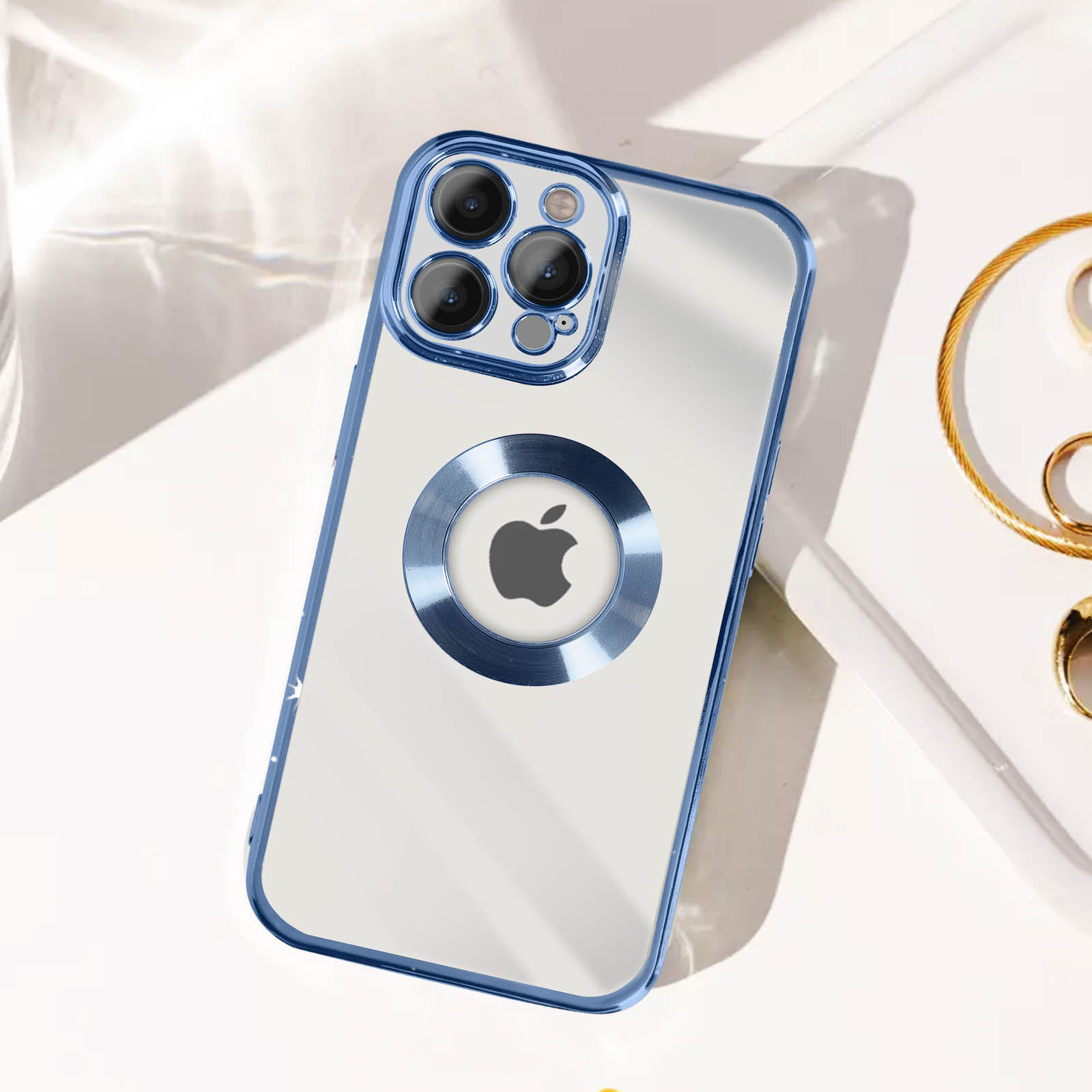 Custodia trasparente con bordo blu, logo Apple. Gioielli d'oro sullo sfondo.