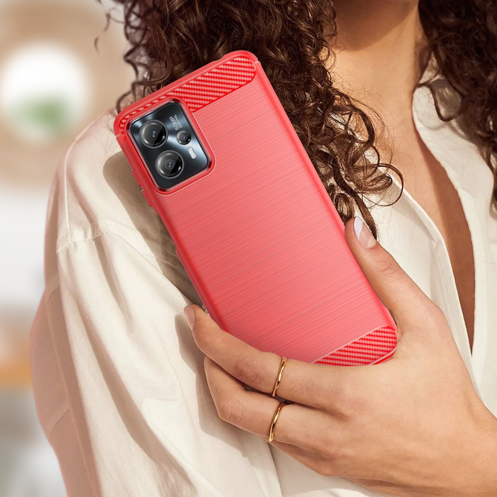 Una custodia rossa su uno smartphone, tenuta da una persona, con camicia bianca e anelli alle dita.