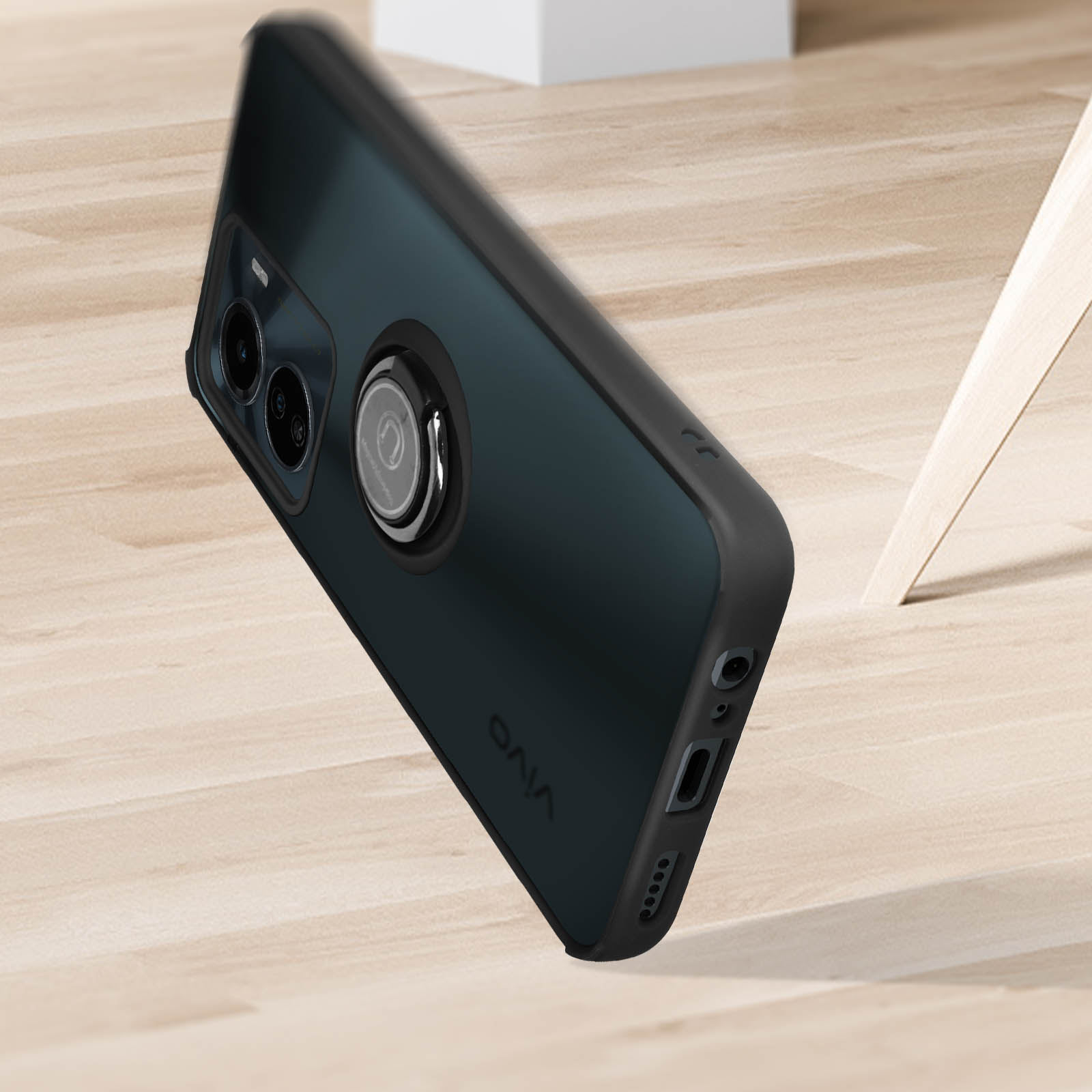 Custodia per telefono nera con supporto ad anello, che cade su una superficie in legno.