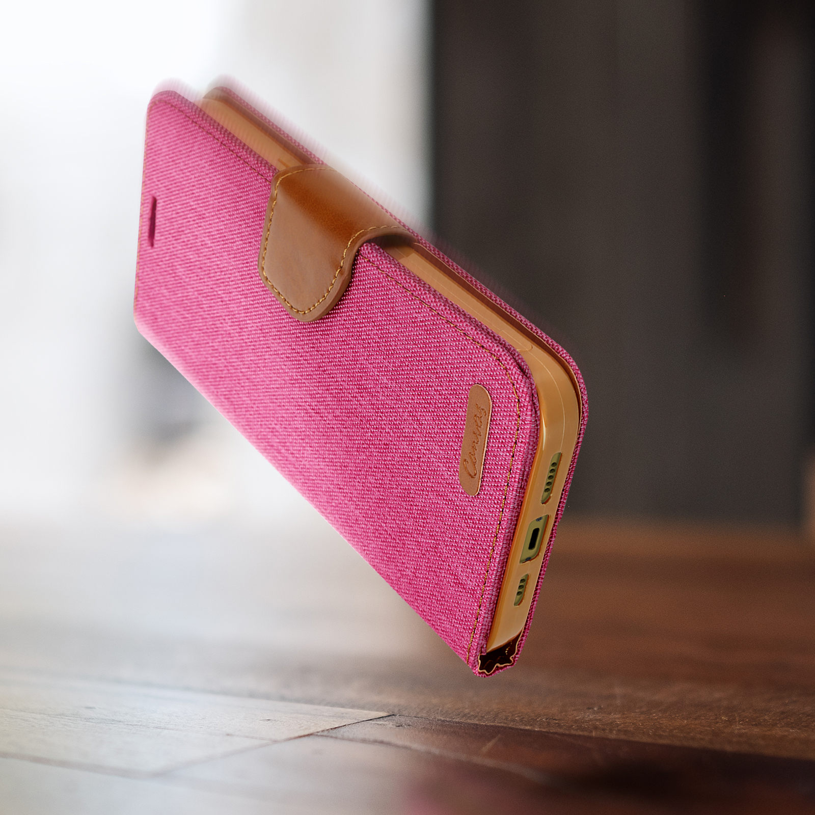 Custodia rosa per telefono con chiusura marrone, appoggiata su una superficie di legno.