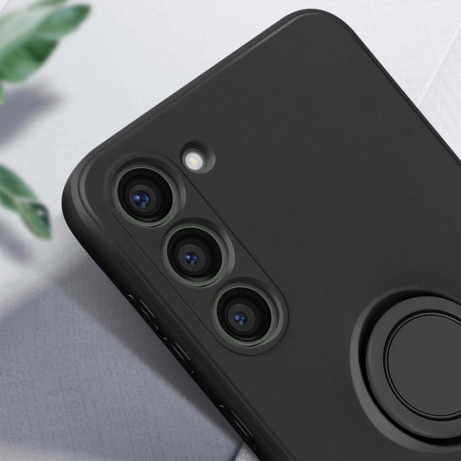 Una custodia per telefono nera con tre lenti della fotocamera e un supporto ad anello. Lo sfondo è sfocato.