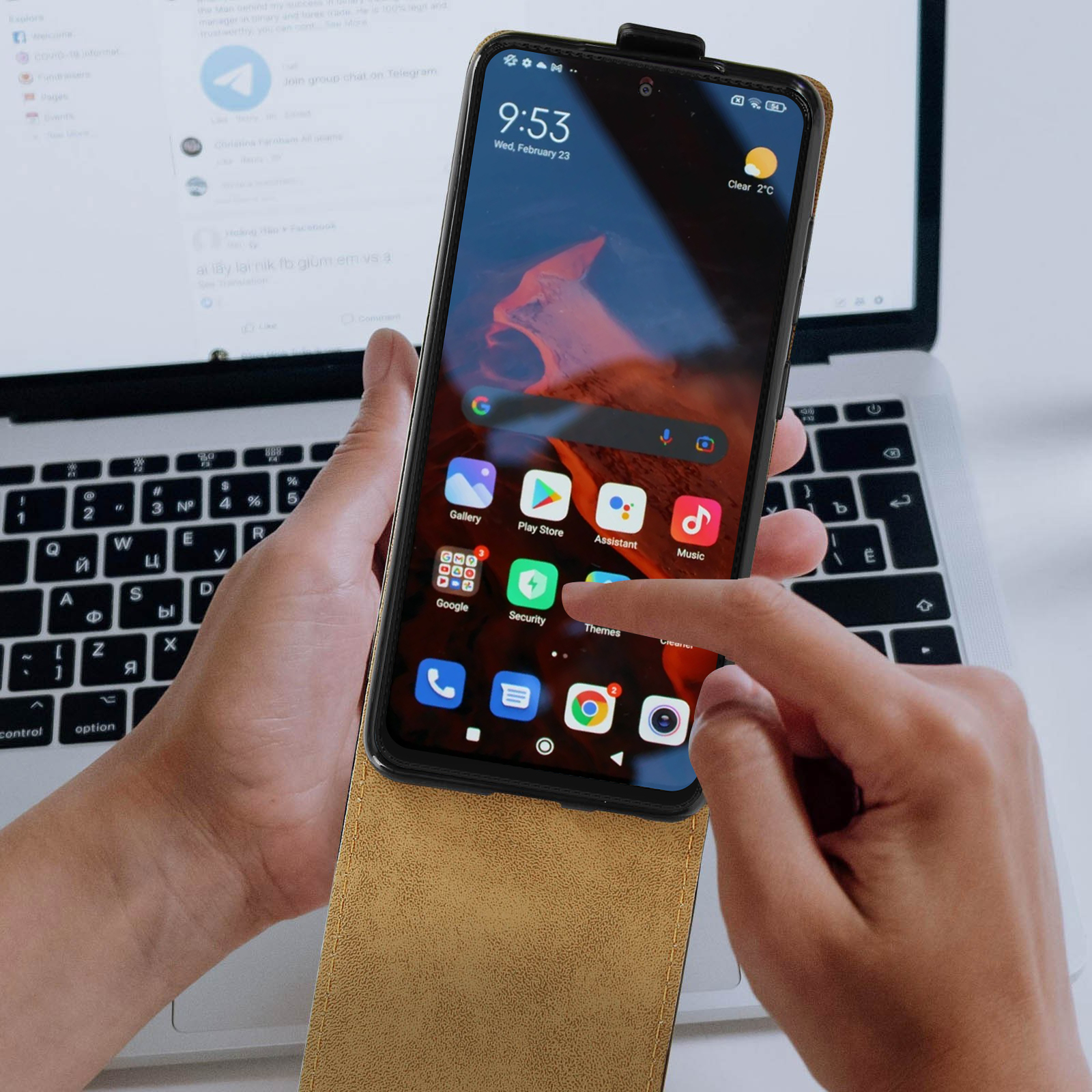 Une main touche un téléphone sur un ordinateur portable. Le téléphone affiche des applications à l'écran.