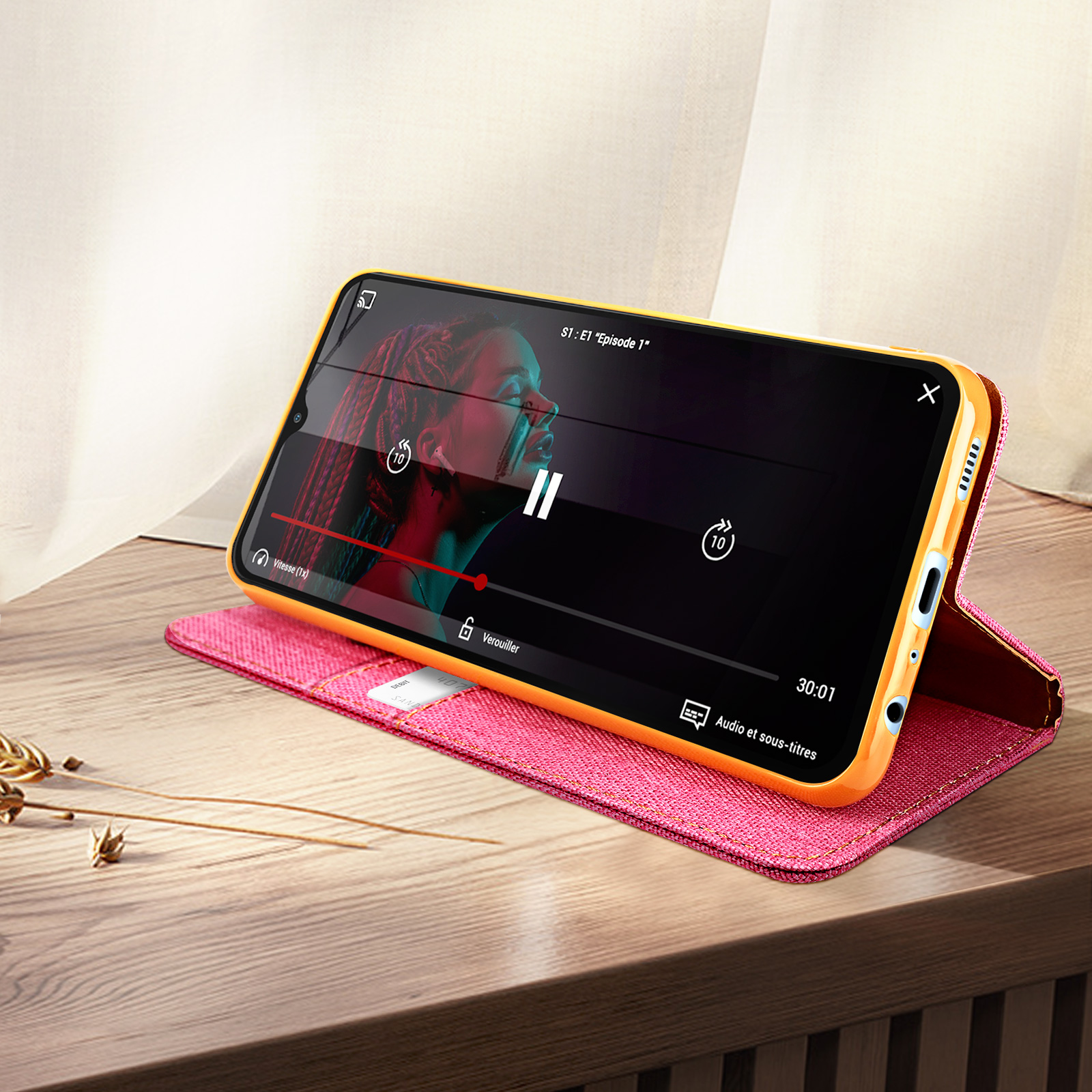 Ein Telefon mit rosa Hülle zeigt ein Video auf seinem Bildschirm. Das Telefon steht auf einer Holzoberfläche.