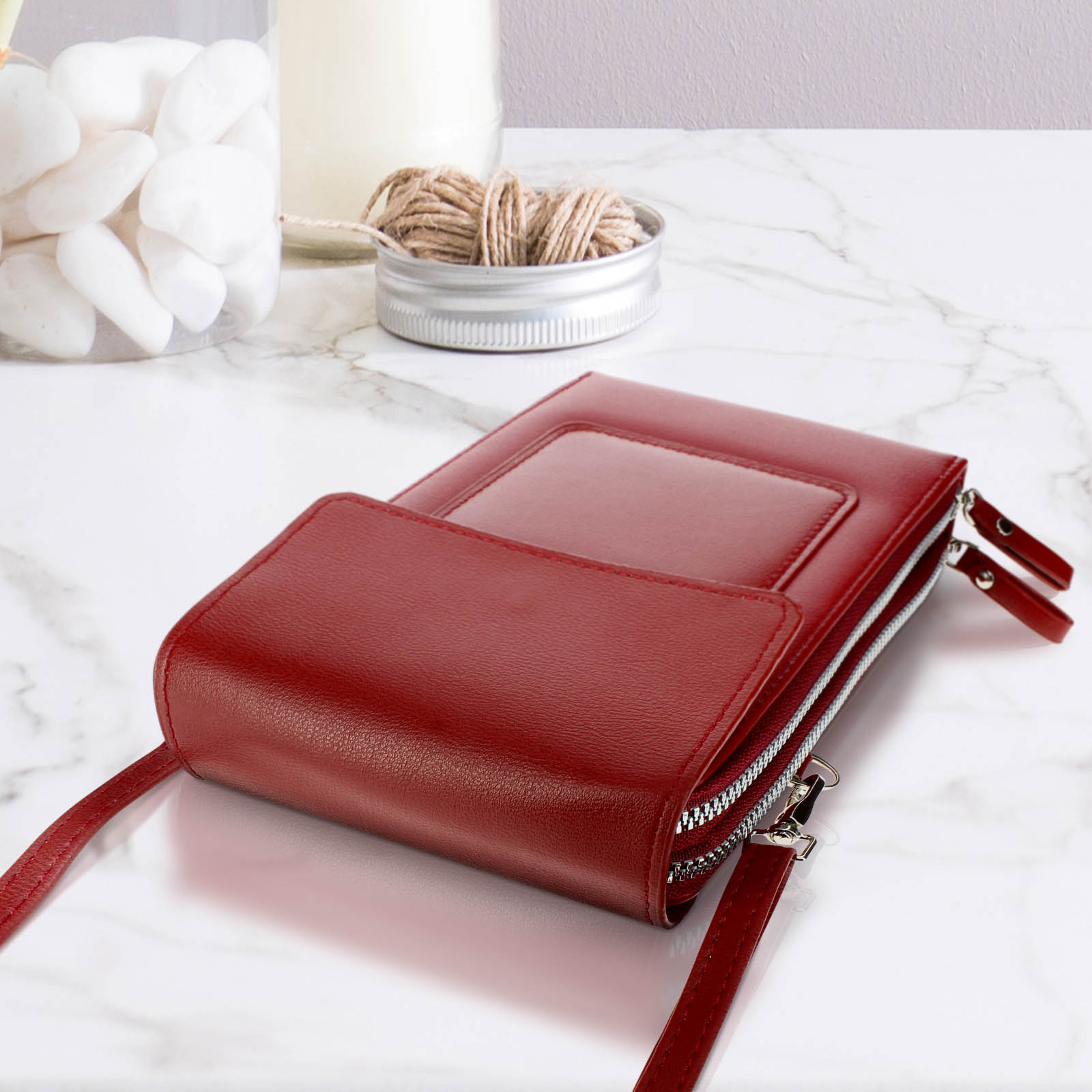 Rotes Leder-Portemonnaie-Handy-Etui mit Reißverschlüssen. Marmoroberfläche, kleiner Behälter mit Garn.