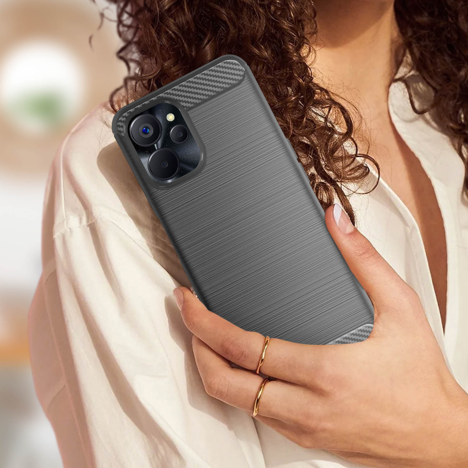 Una donna tiene in mano un telefono con una custodia grigia. La custodia ha una parte superiore in fibra di carbonio ed è su una camicia bianca.