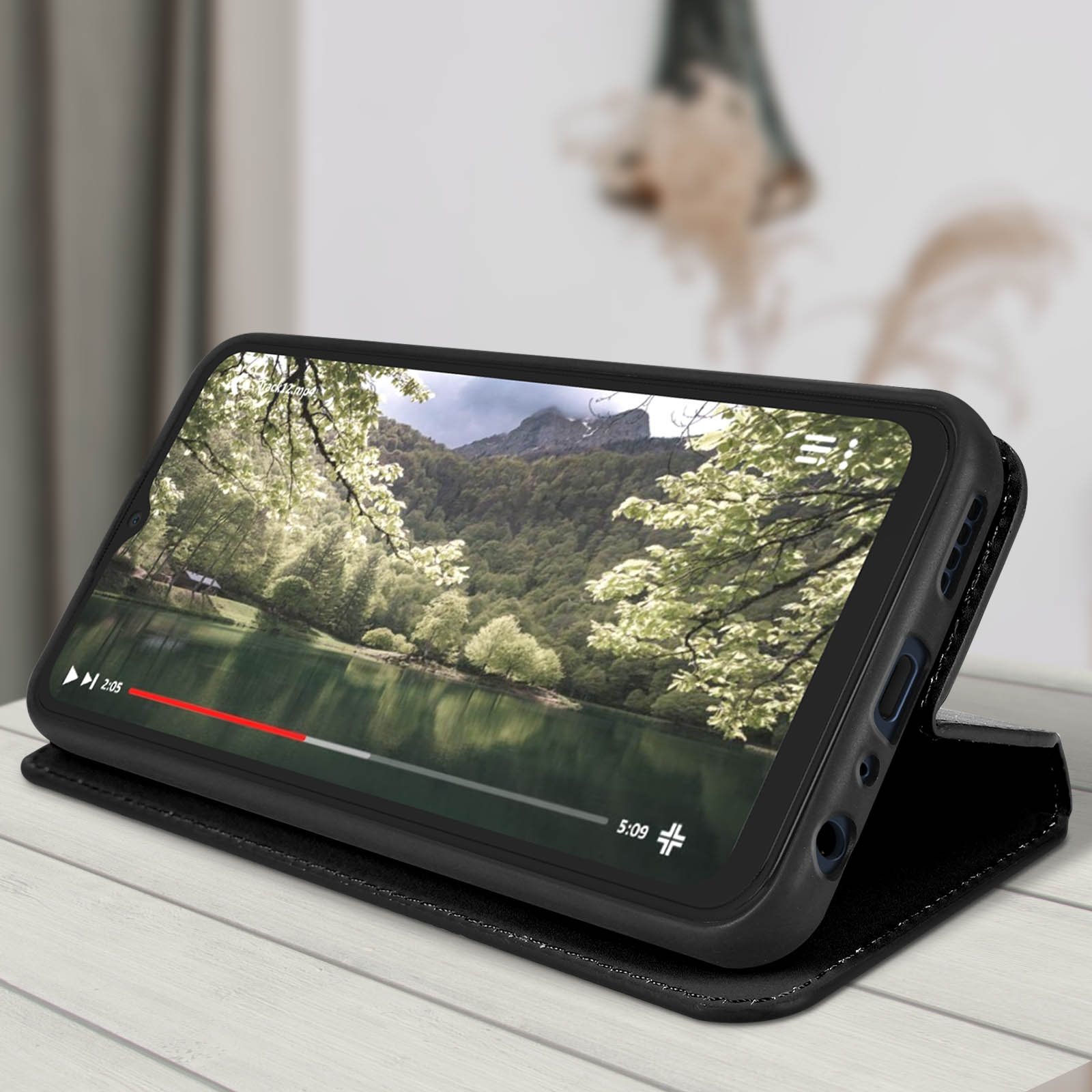 Telefon zeigt Video, schwarzes Gehäuse, offen liegend, Szene von See und Bäumen.