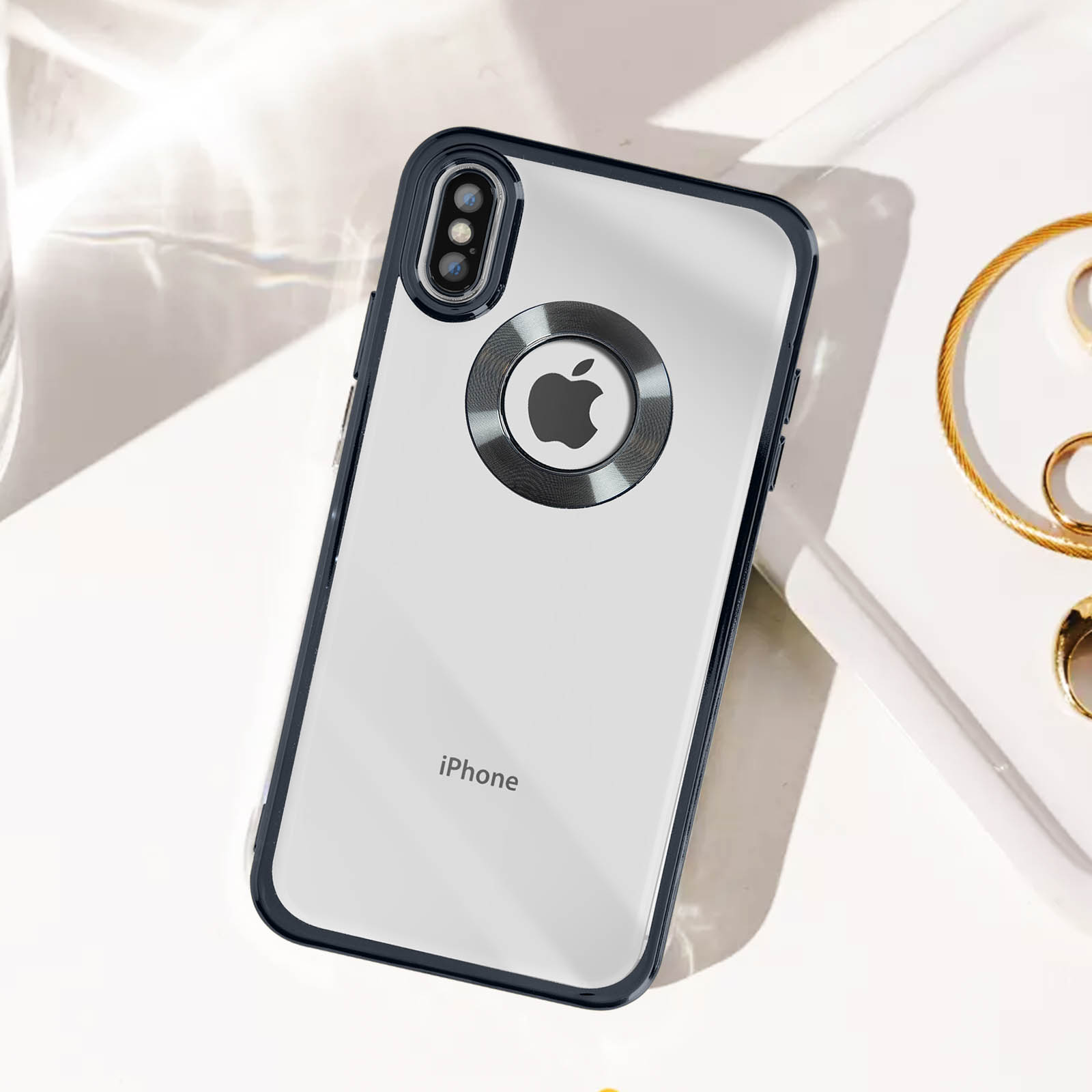 iPhone in custodia trasparente con bordi neri, logo e anello Apple argentati, su superficie bianca.