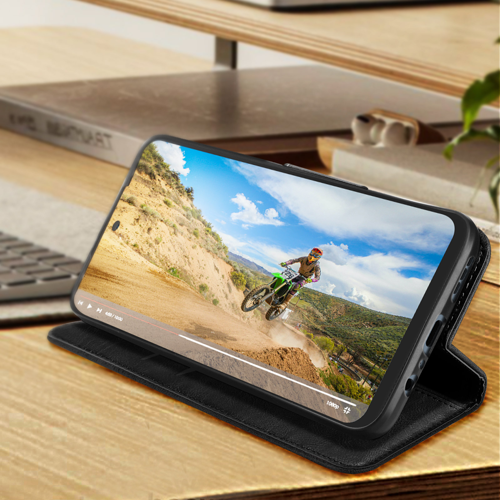 Un telefono in una custodia a portafoglio sta riproducendo un video di motocross. La custodia è su una scrivania di legno.
