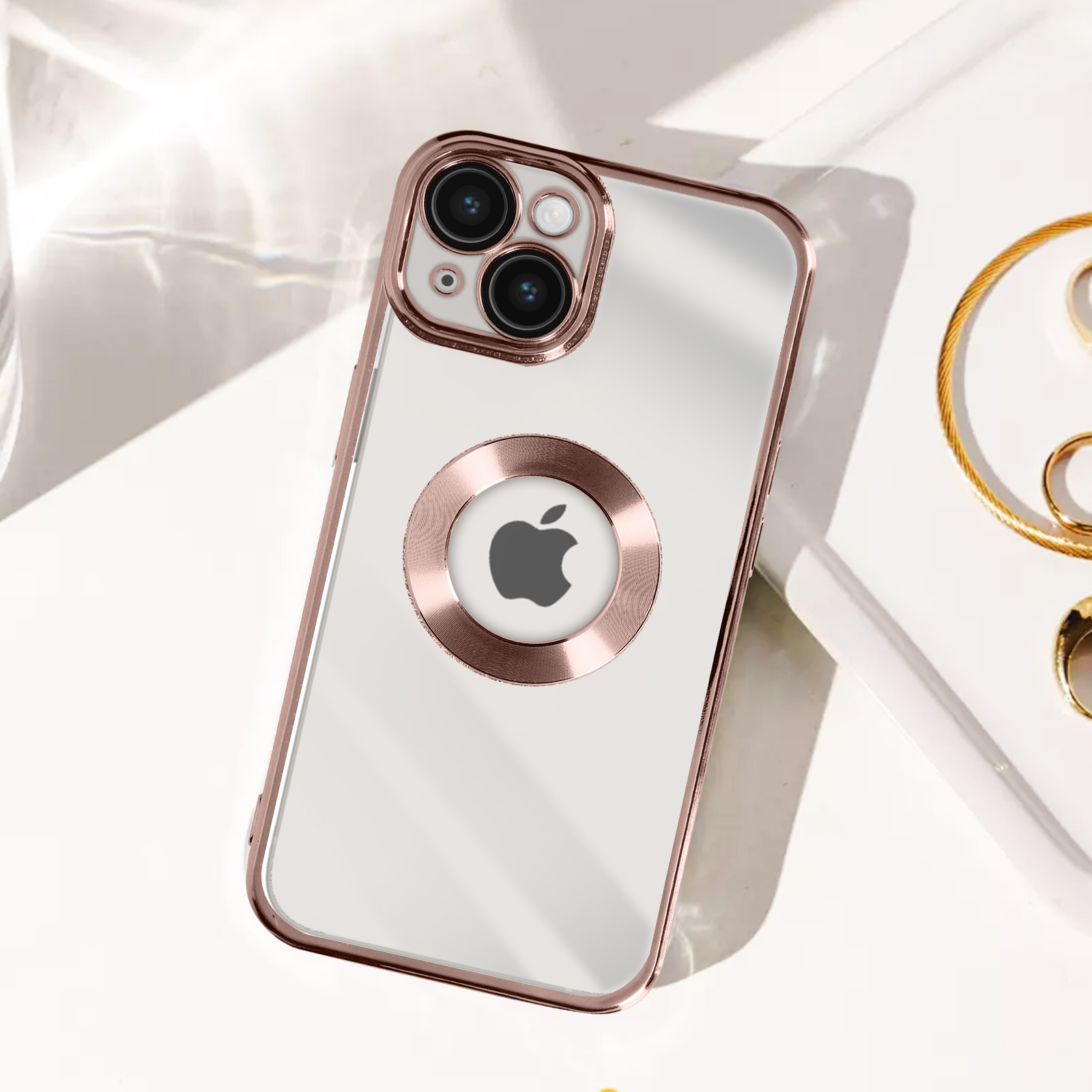 Custodia trasparente con finiture oro rosa, che tiene un iPhone. Gioielli a destra.