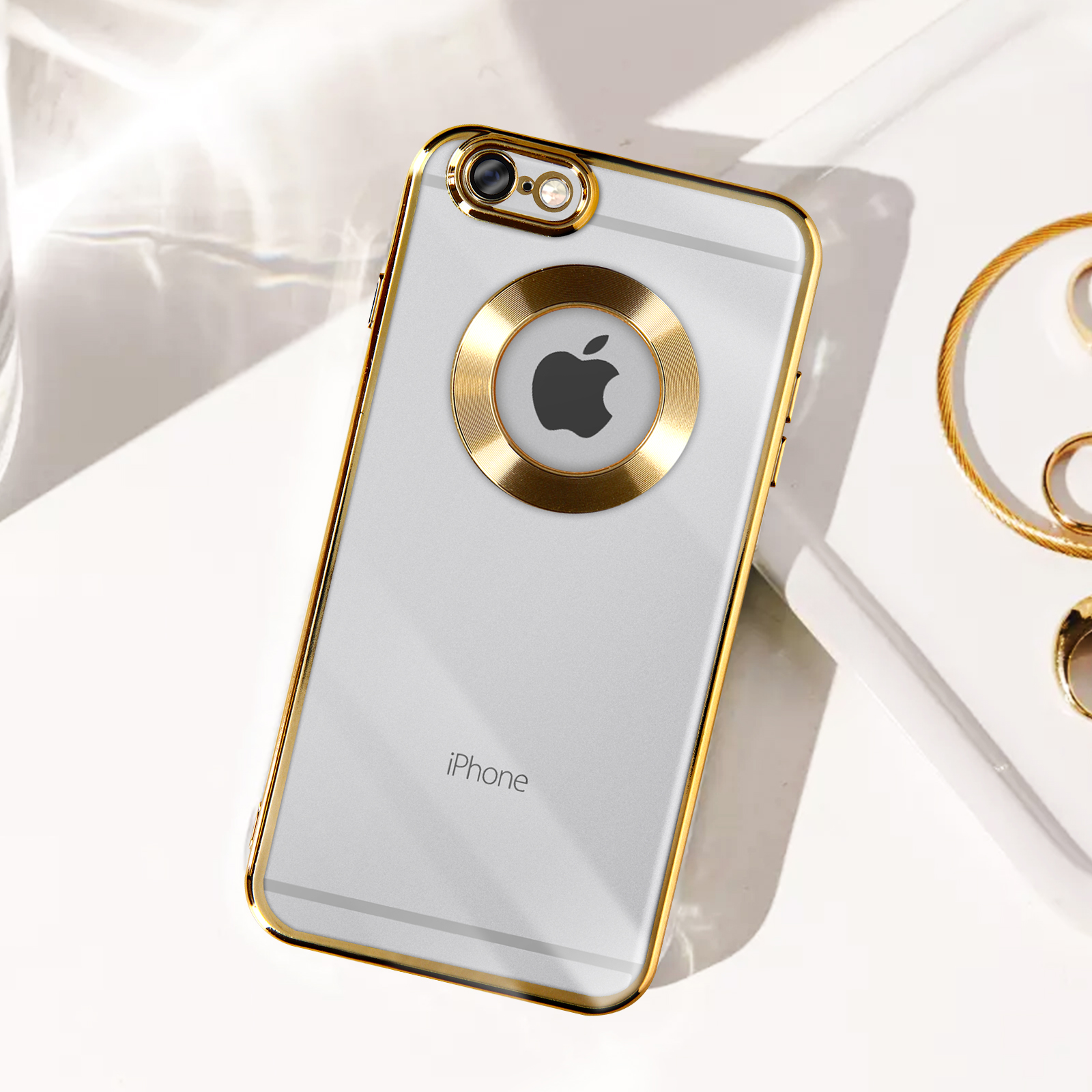 Un teléfono con marco dorado con un círculo dorado alrededor del logotipo de Apple. Una pulsera dorada sobre la superficie blanca.
