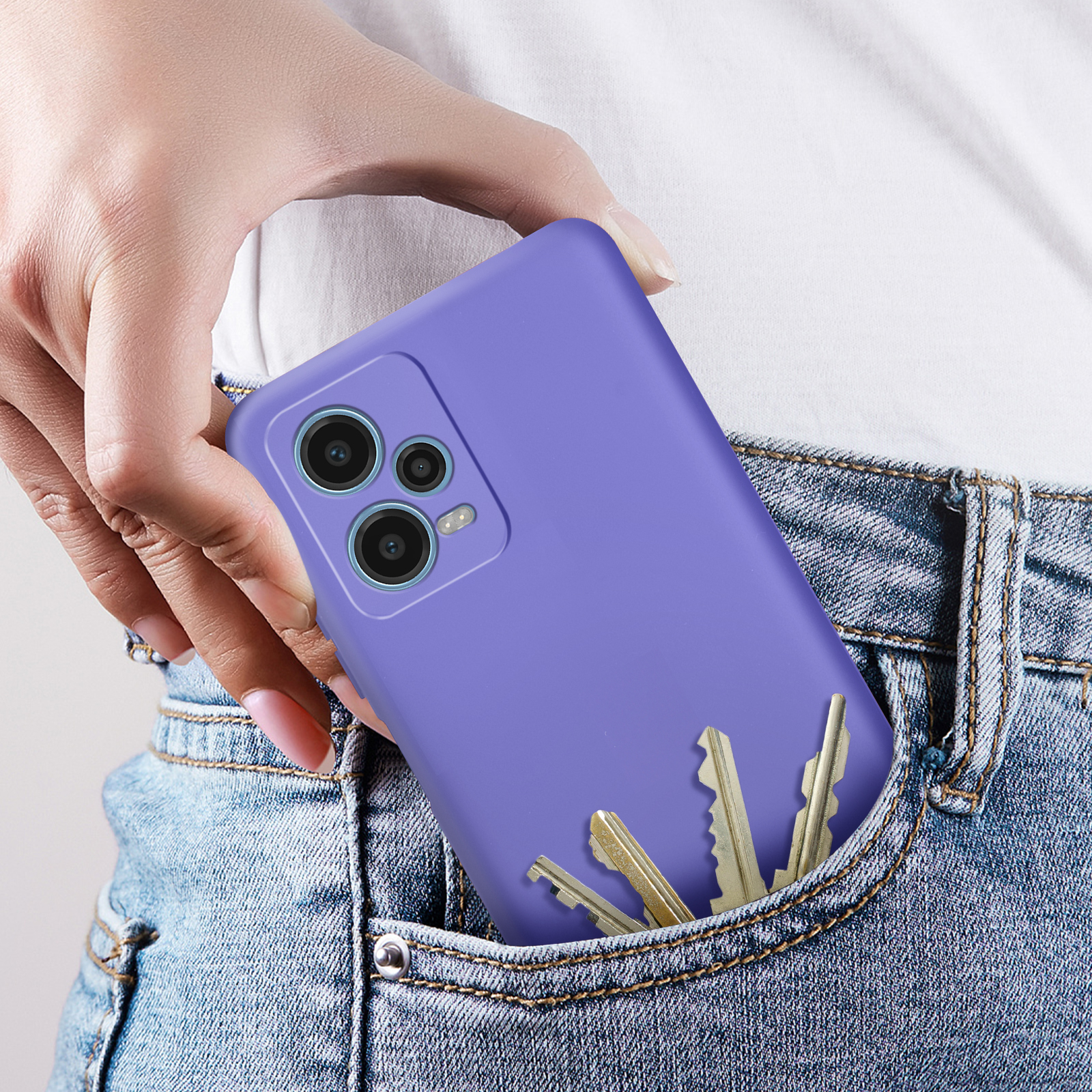 Mano di una persona che tiene un telefono viola in una tasca di jeans con chiavi.