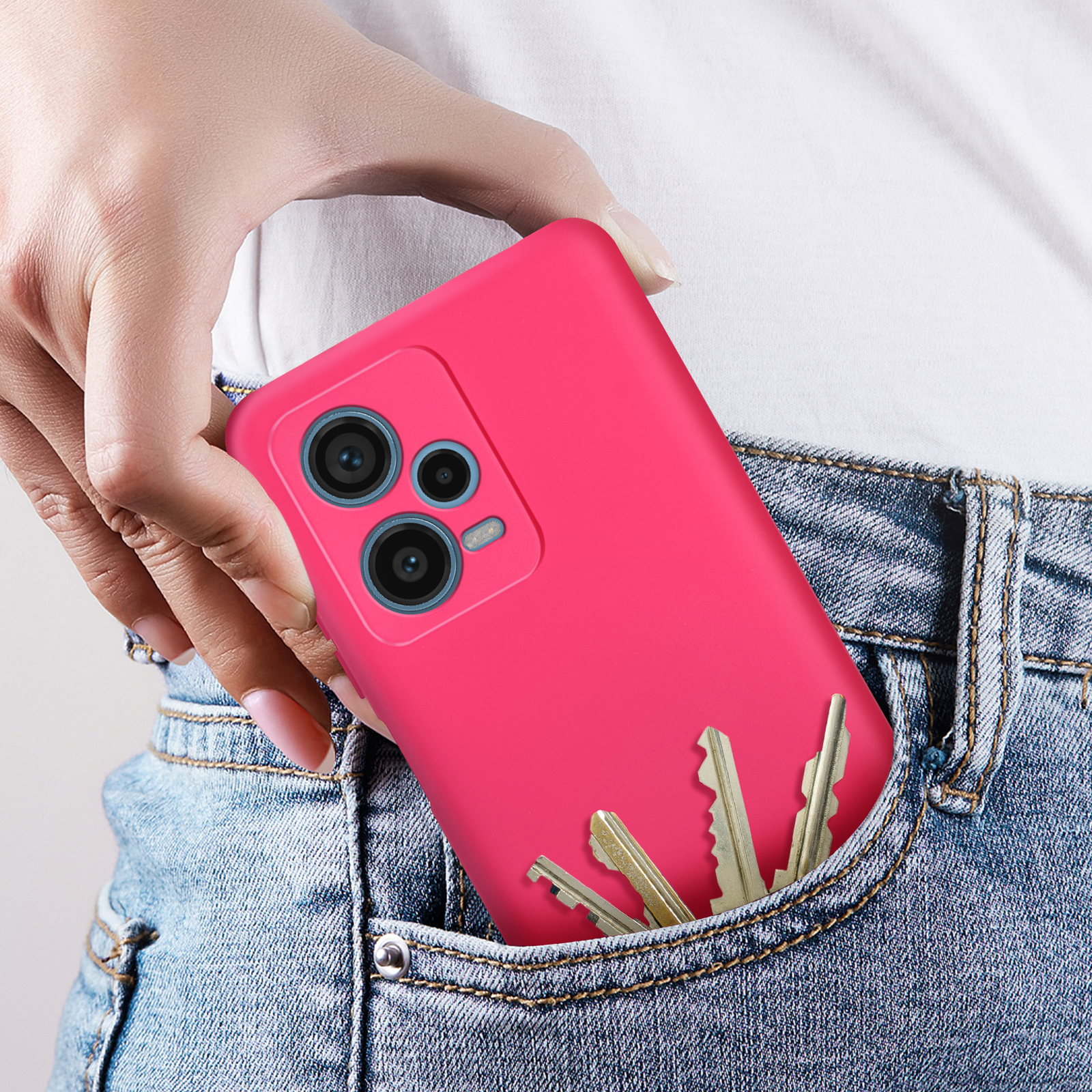 Mano che tiene un telefono rosa in tasca con chiavi. Jeans, camicia bianca.
