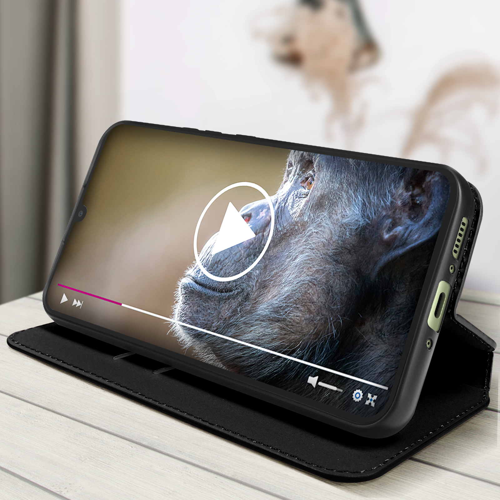 Téléphone dans un étui noir affichant une vidéo de chimpanzé, un bouton de lecture visible.