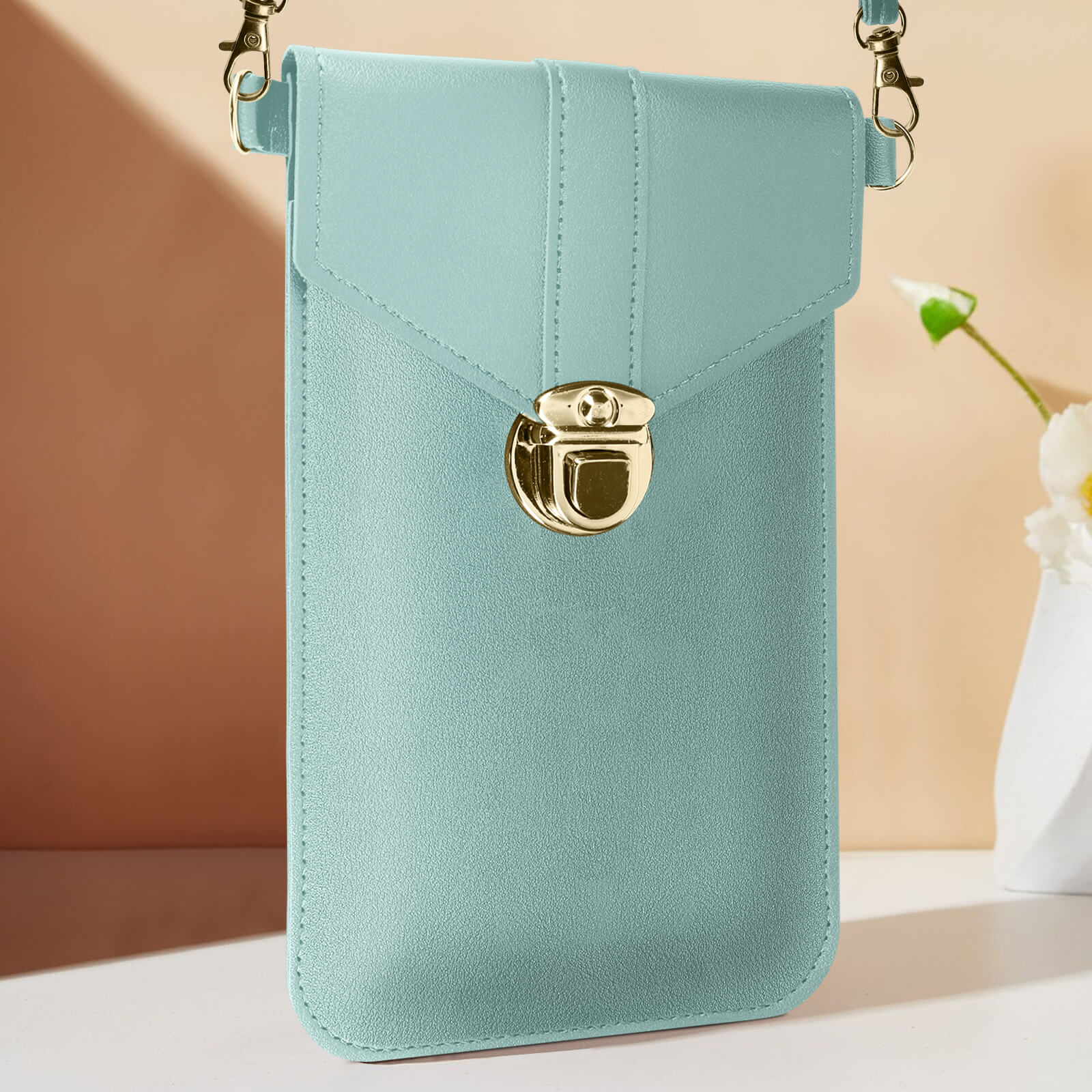 Una borsa per telefono azzurra con chiusura e catena dorate. La borsa è appesa su uno sfondo marrone chiaro.
