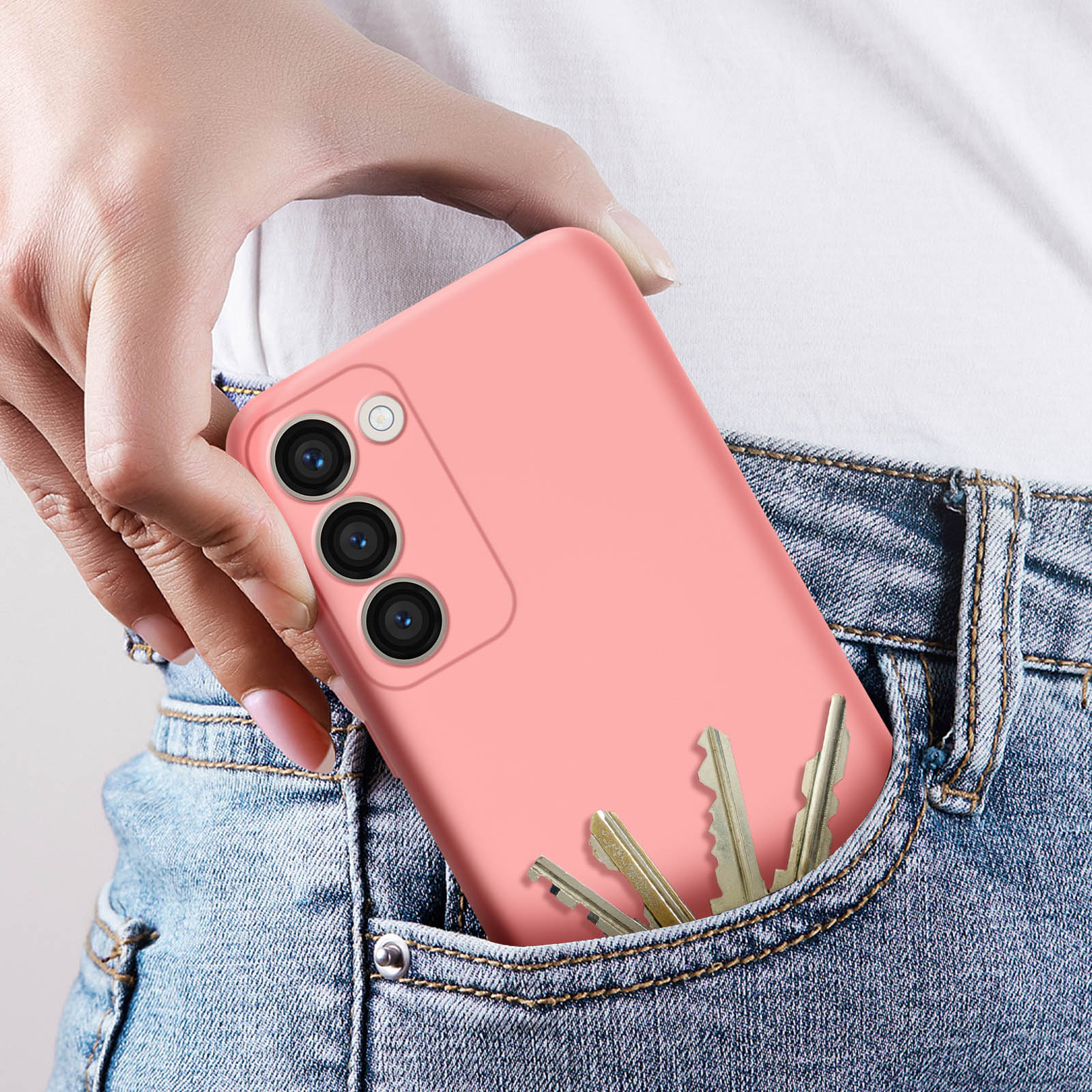 Una mano di donna che mette un telefono con una custodia rosa in una tasca dei jeans. Anche alcune chiavi sono in tasca.