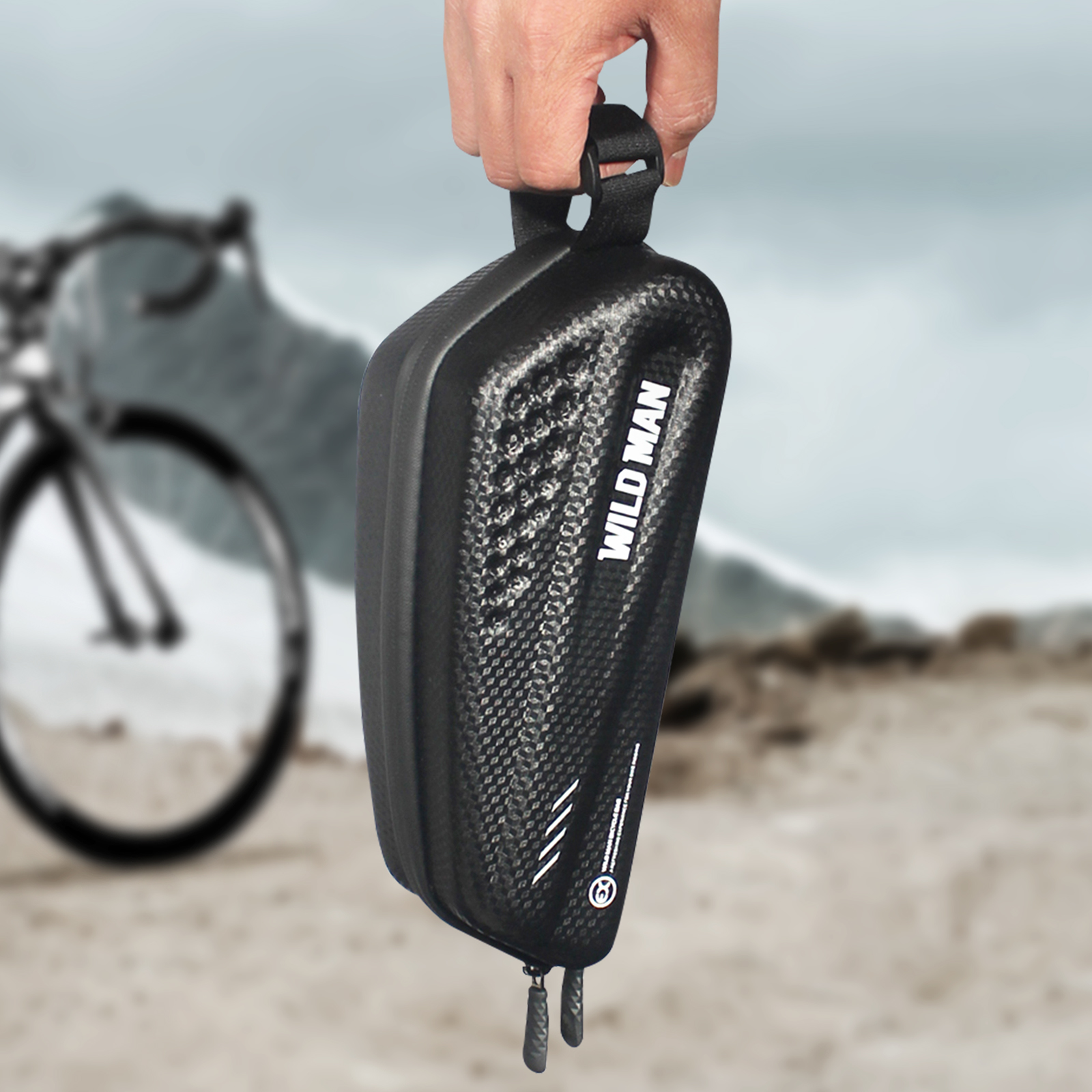 Hand hält eine schwarze Fahrradtasche, mit Fahrrad und Bergkulisse. 'WILD MAN' auf der Tasche.
