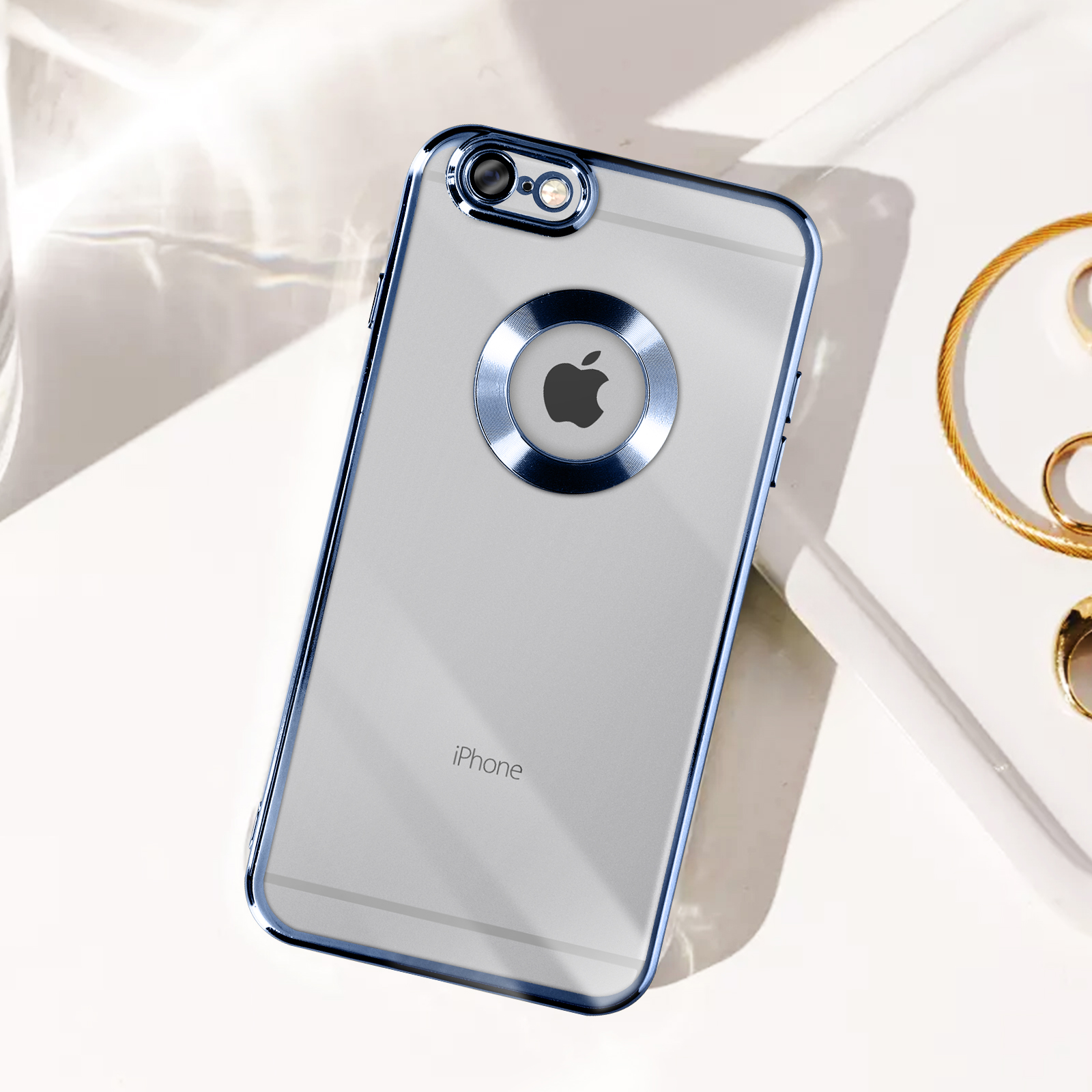 Custodia trasparente per iPhone con bordi blu su superficie bianca, gioielli d'oro sullo sfondo.