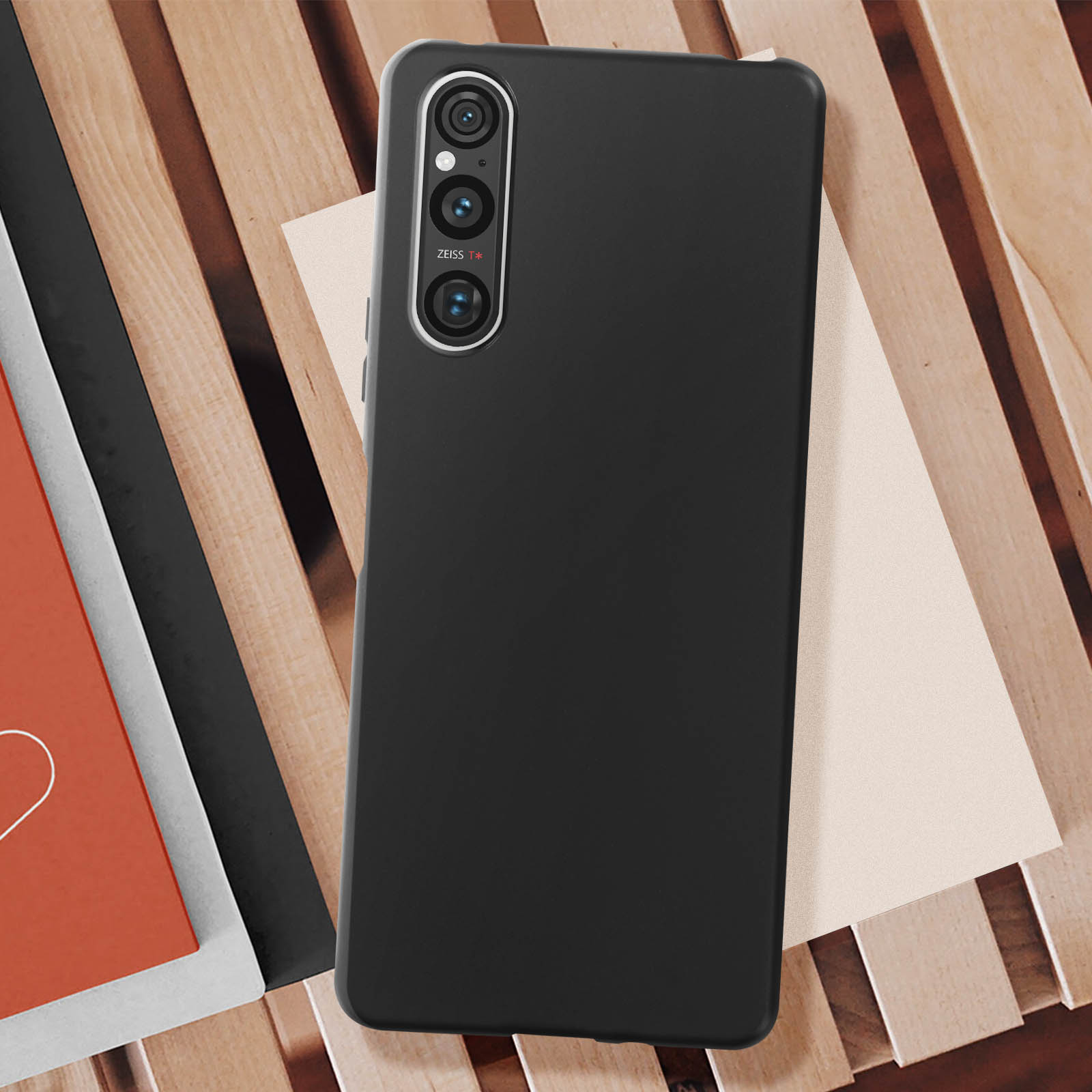Telefono nero con tripla fotocamera su doghe di legno, con libri e carta.