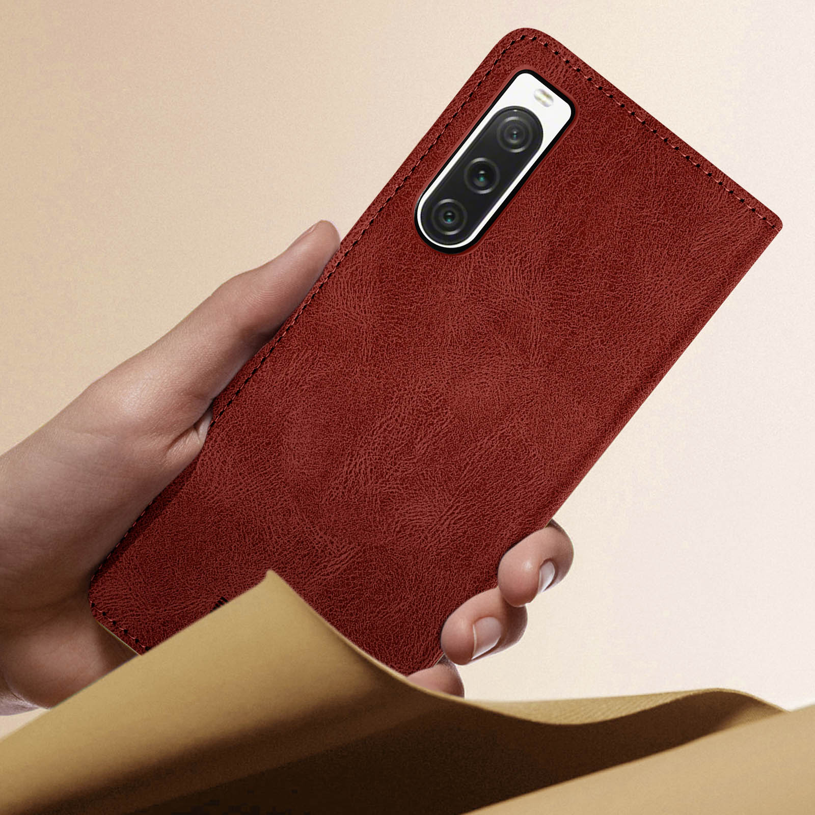 Eine Hand hält eine braune Handyhülle mit einem Telefon darin, auf einer Oberfläche liegend.