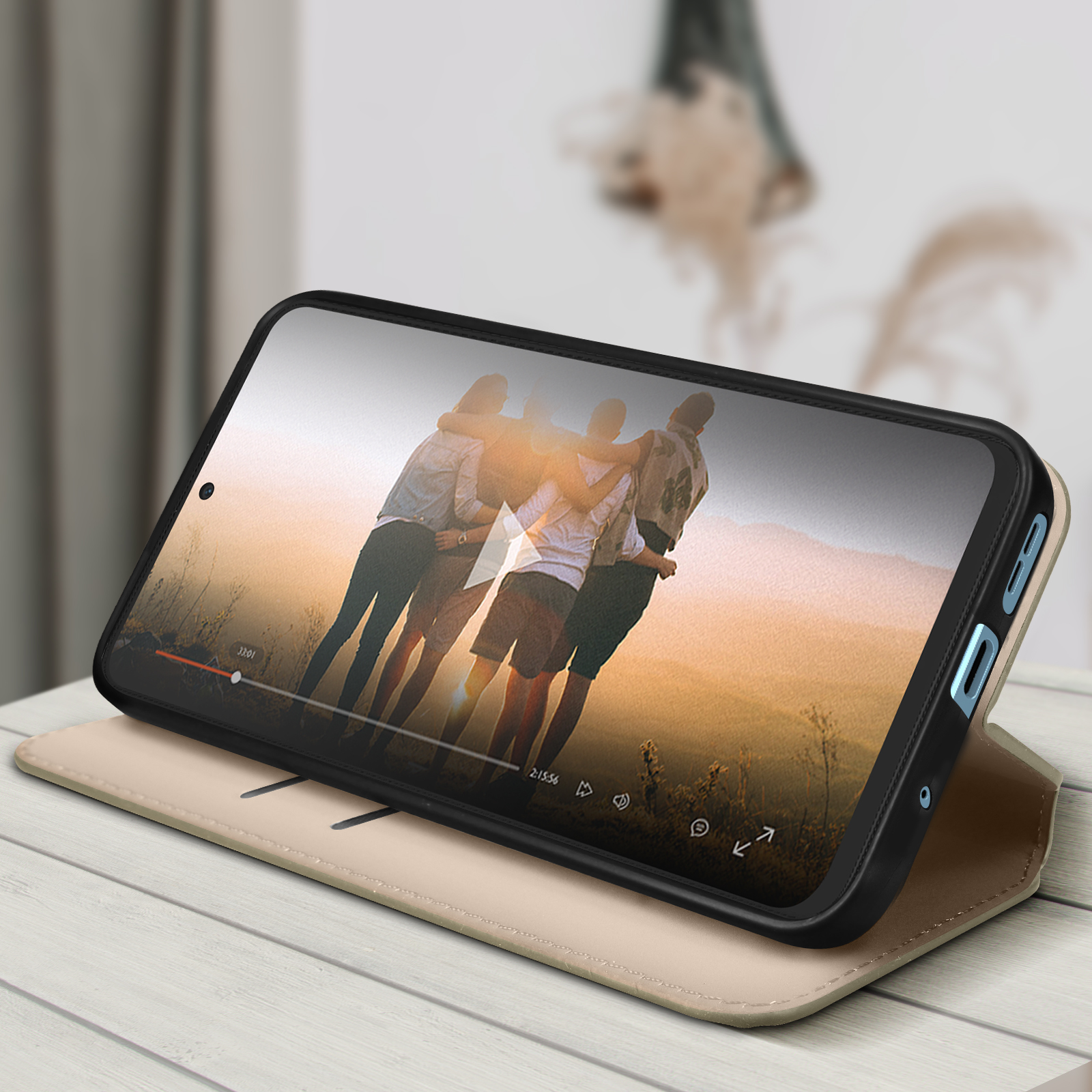 Telefono con video, custodia aperta. Persone nel video. Tavolo e pianta sullo sfondo.
