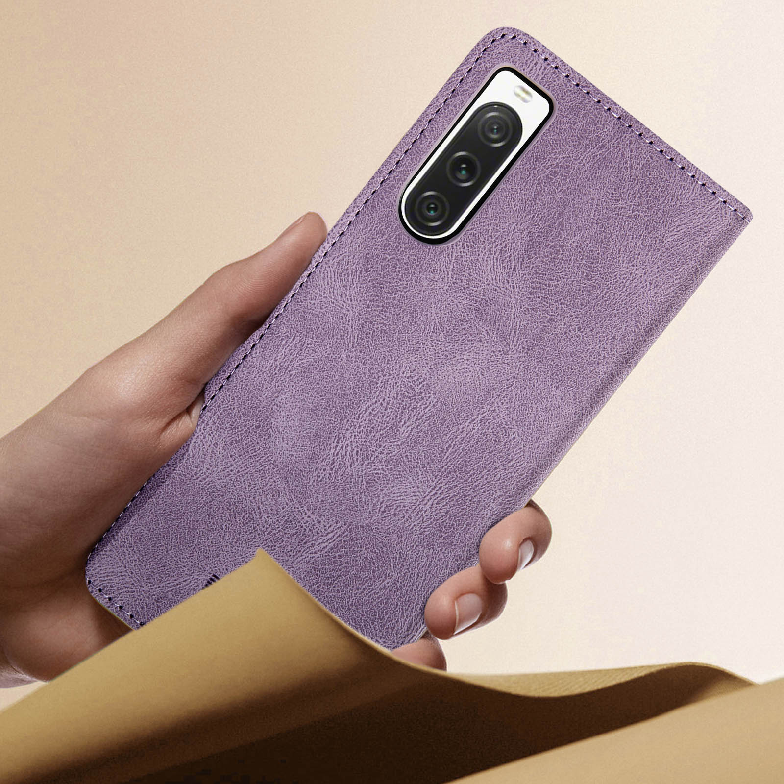 Mano che tiene una custodia viola effetto pelle. Il retro della custodia è visibile. Sfondo sfocato.
