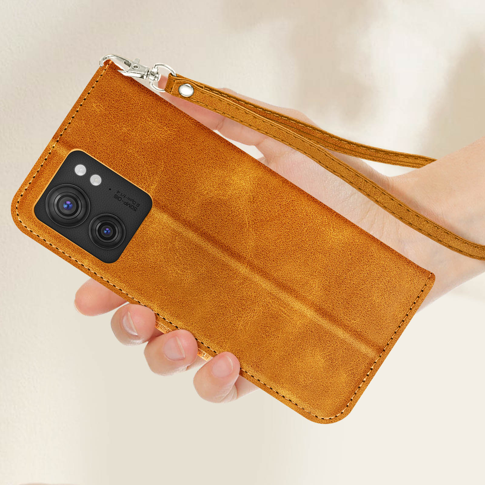 Una mano tiene in mano una custodia per telefono in pelle marrone stile portafoglio con un cinturino da polso.