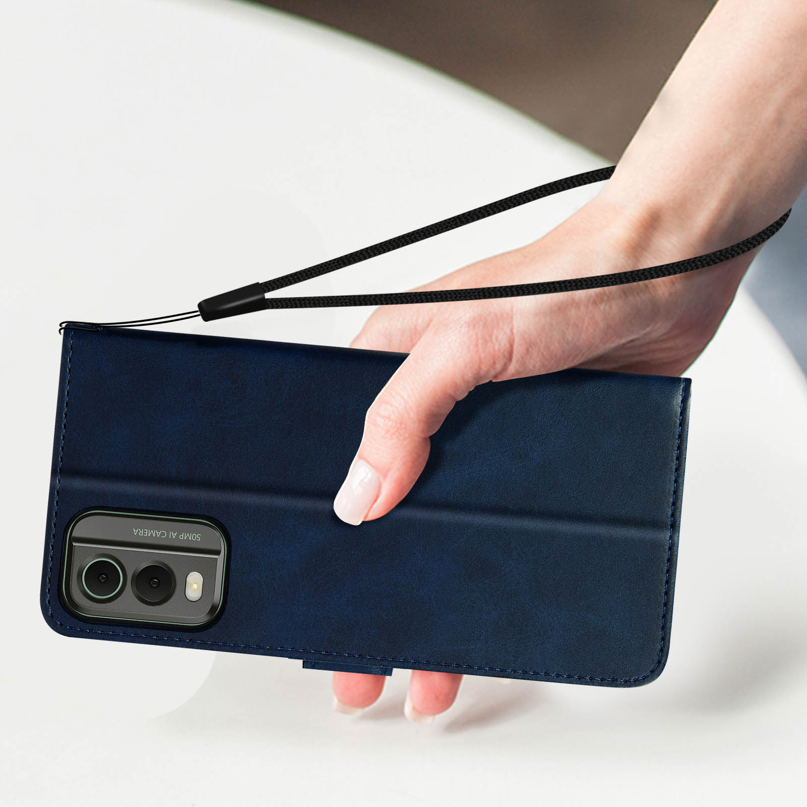 Una mano che tiene una custodia per telefono blu navy con un cinturino. La custodia ha una fotocamera. Sfondo bianco.