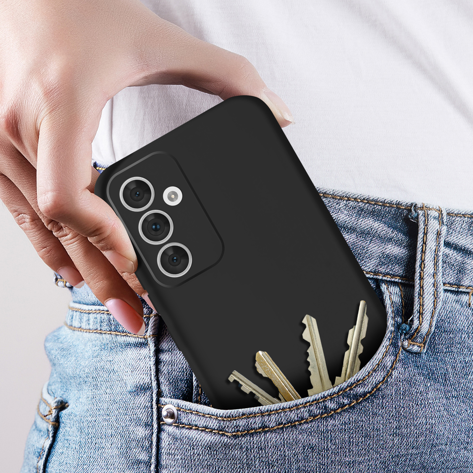 Hand hält ein schwarzes Telefon in einer Tasche. Drei Schlüssel sind ebenfalls in der Tasche. Jeans werden getragen.