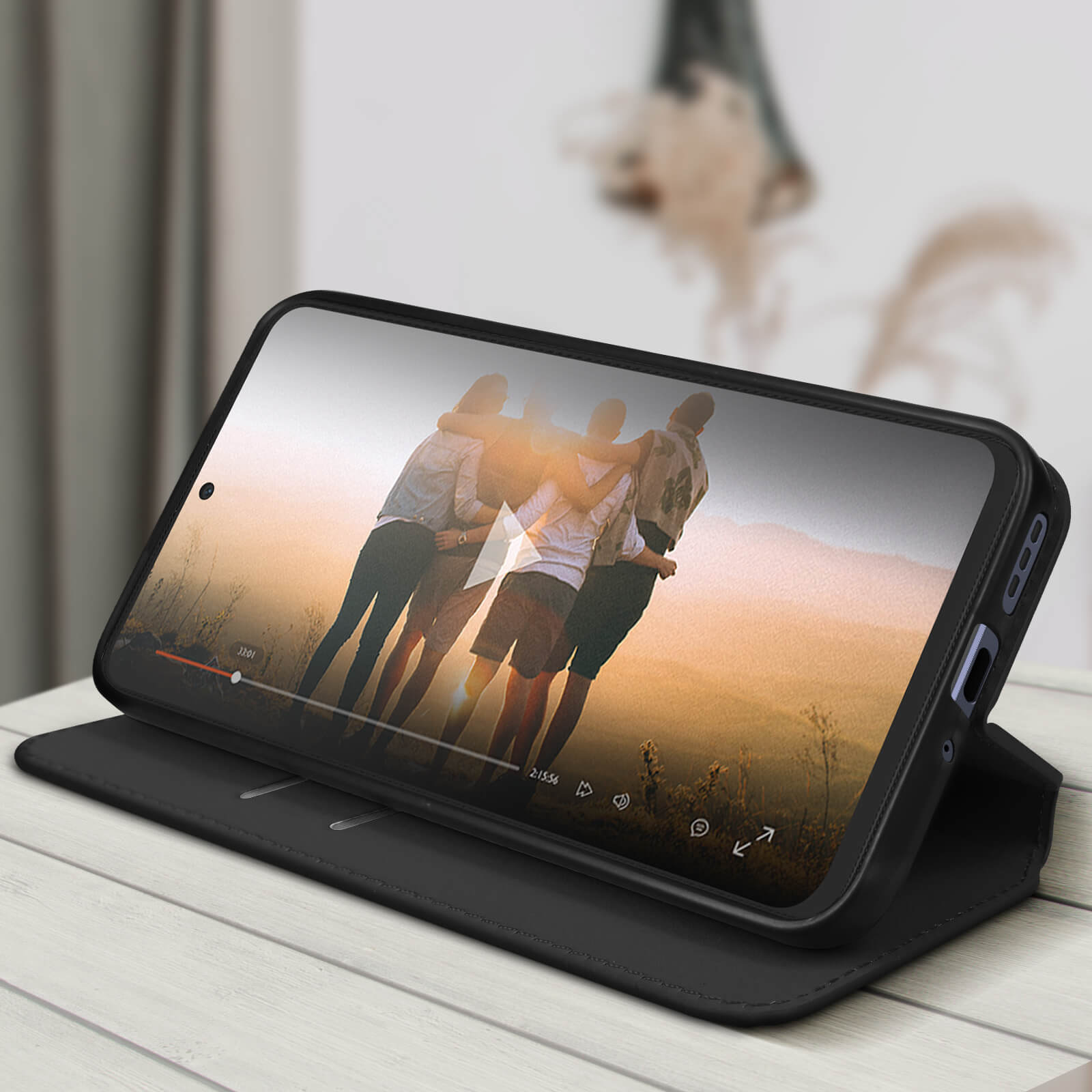 Il telefono su supporto mostra video di persone. Custodia nera su un tavolo di legno.