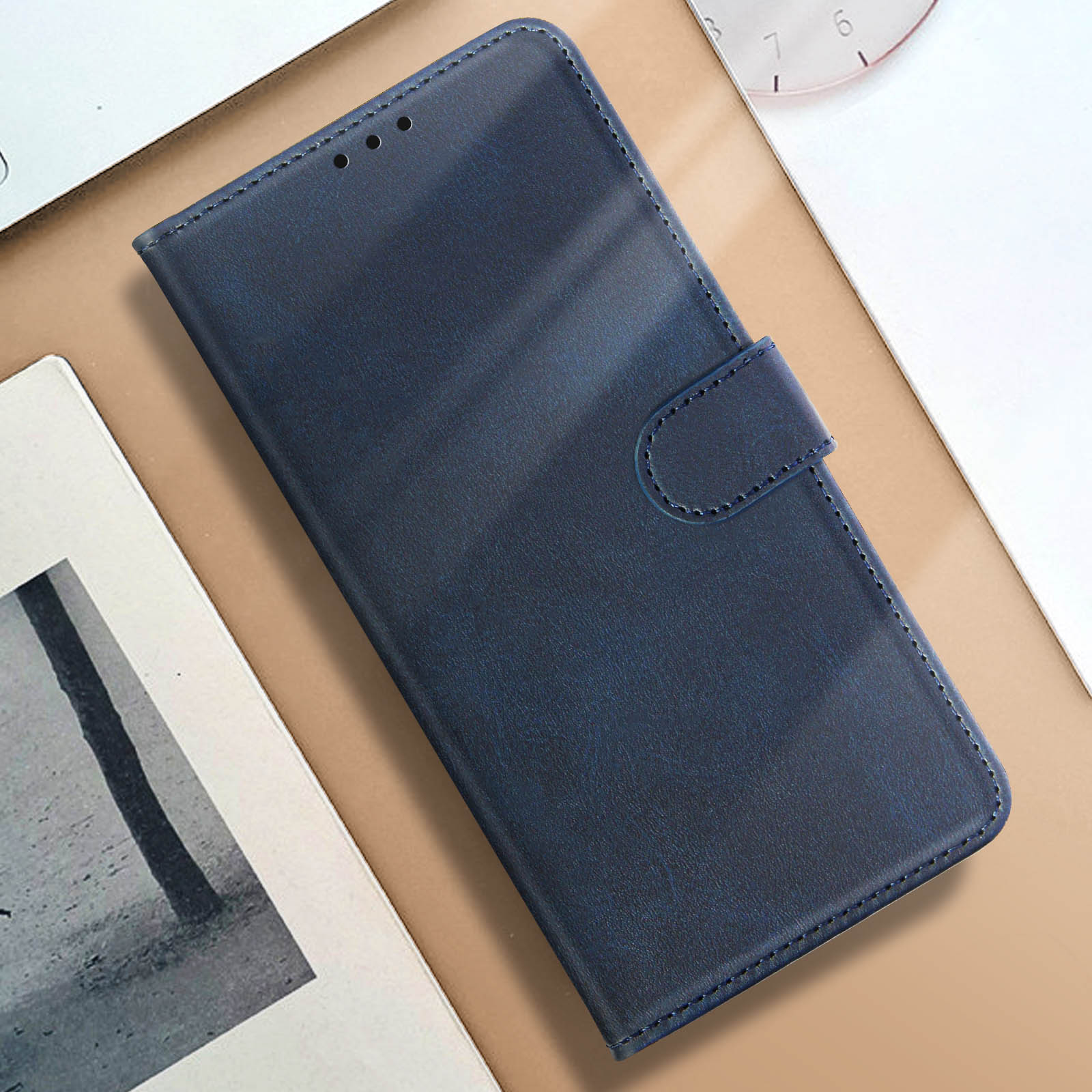 Custodia per telefono in pelle blu, aperta. La custodia è su una superficie beige. Orologio e carta sullo sfondo.