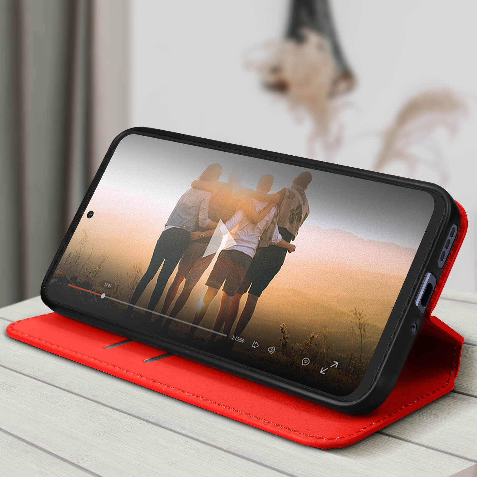 Telefono in custodia rossa, mostra video di persone all'aperto. Custodia rossa aperta su tavolo di legno.