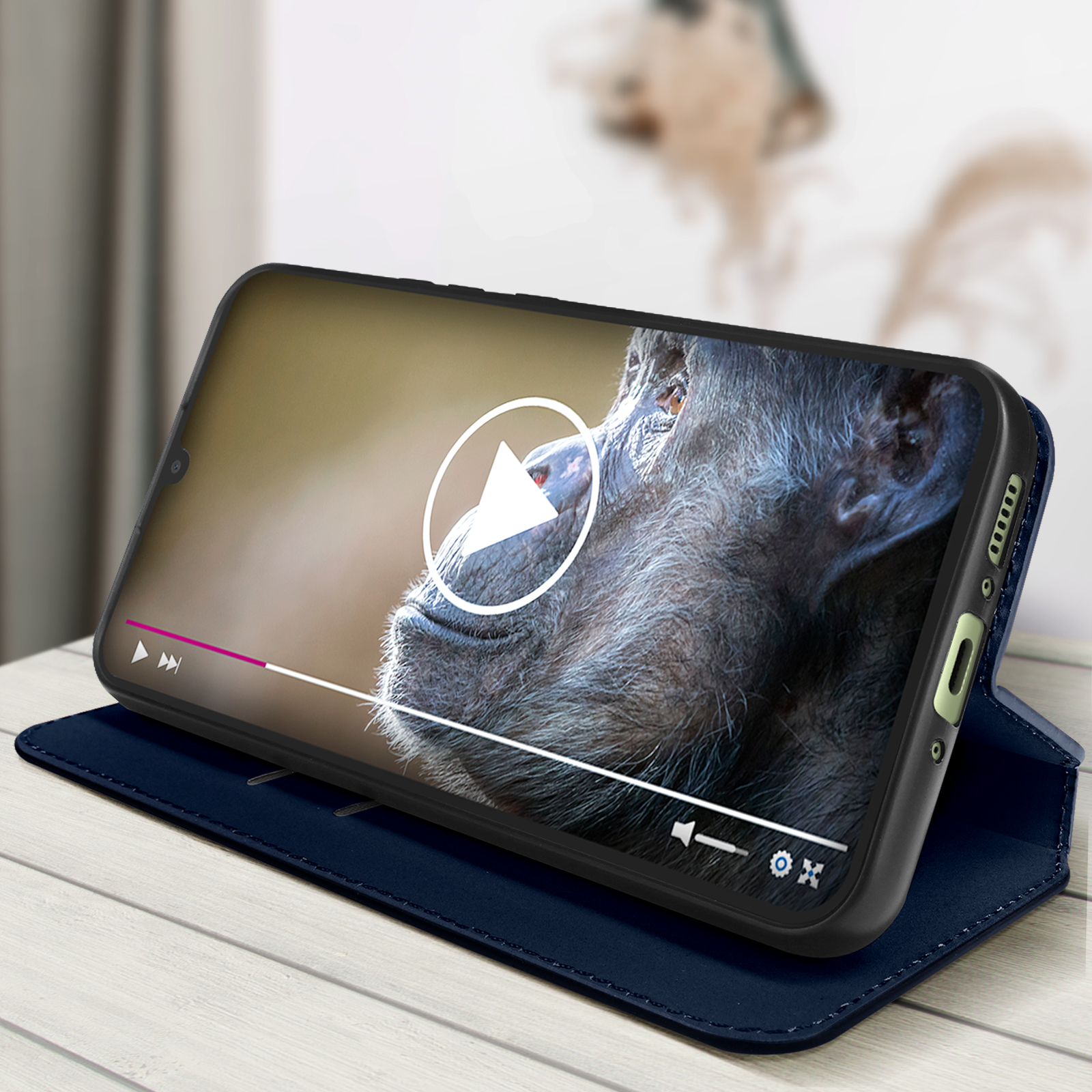 Telefono in una custodia blu, che riproduce un video di uno scimpanzé. Tavolo di legno sullo sfondo.