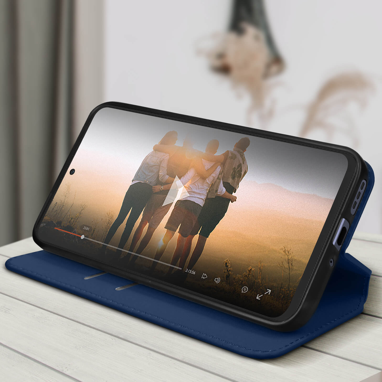 Ein Telefon zeigt ein Video mit Personen. Blaue Lederhülle offen. Holziger Hintergrund.