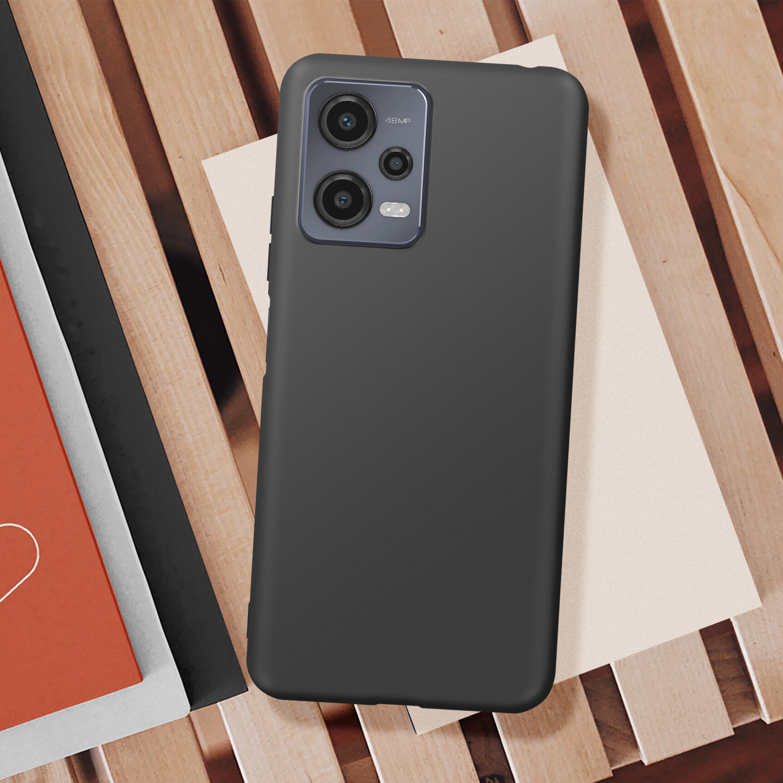 Telefono nero su una superficie di legno. Il telefono poggia su carta bianca e rossa. Fotocamera visibile.