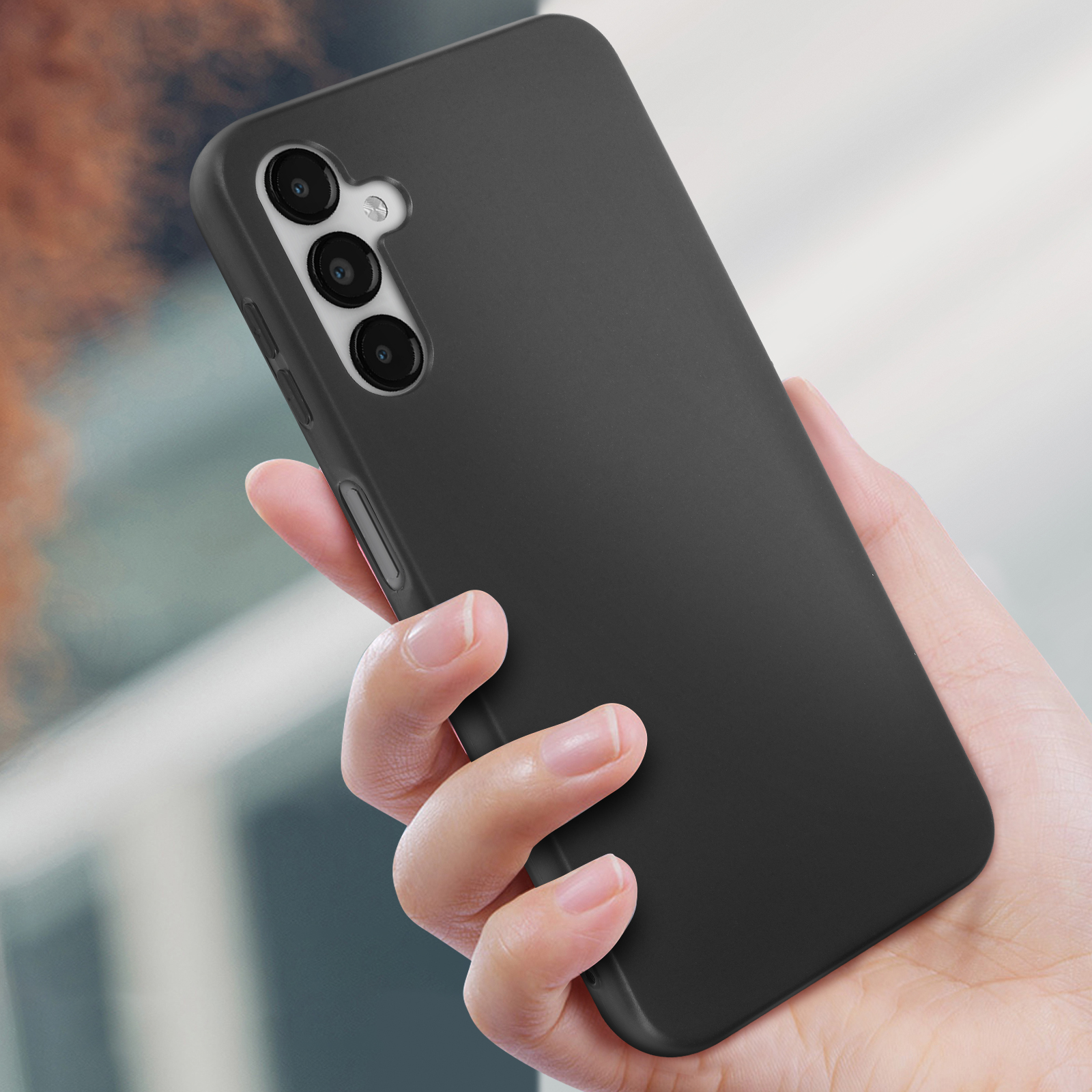Mano che tiene una custodia nera per telefono con tre fotocamere. Il telefono è nero. Sfondo sfocato.