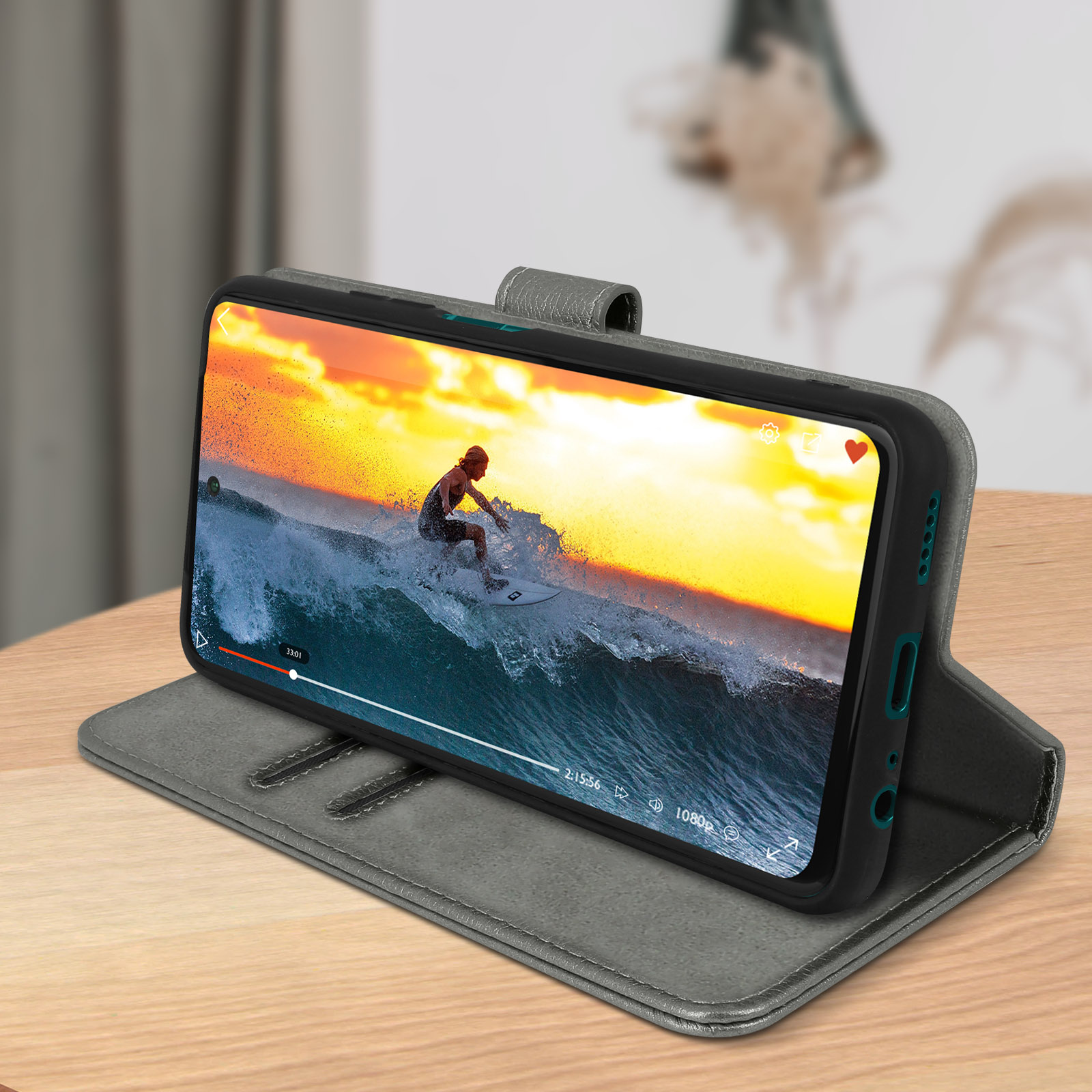 Un telefono in una custodia grigia che riproduce un video di un surfista su un'onda, appoggiato su un tavolo.