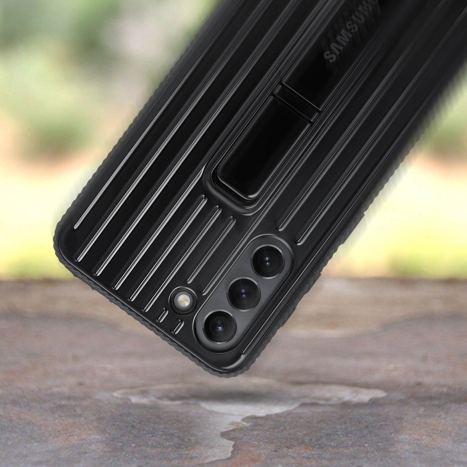 Funda de teléfono negra con soporte. Está sobre una superficie, con una superficie metálica texturizada.