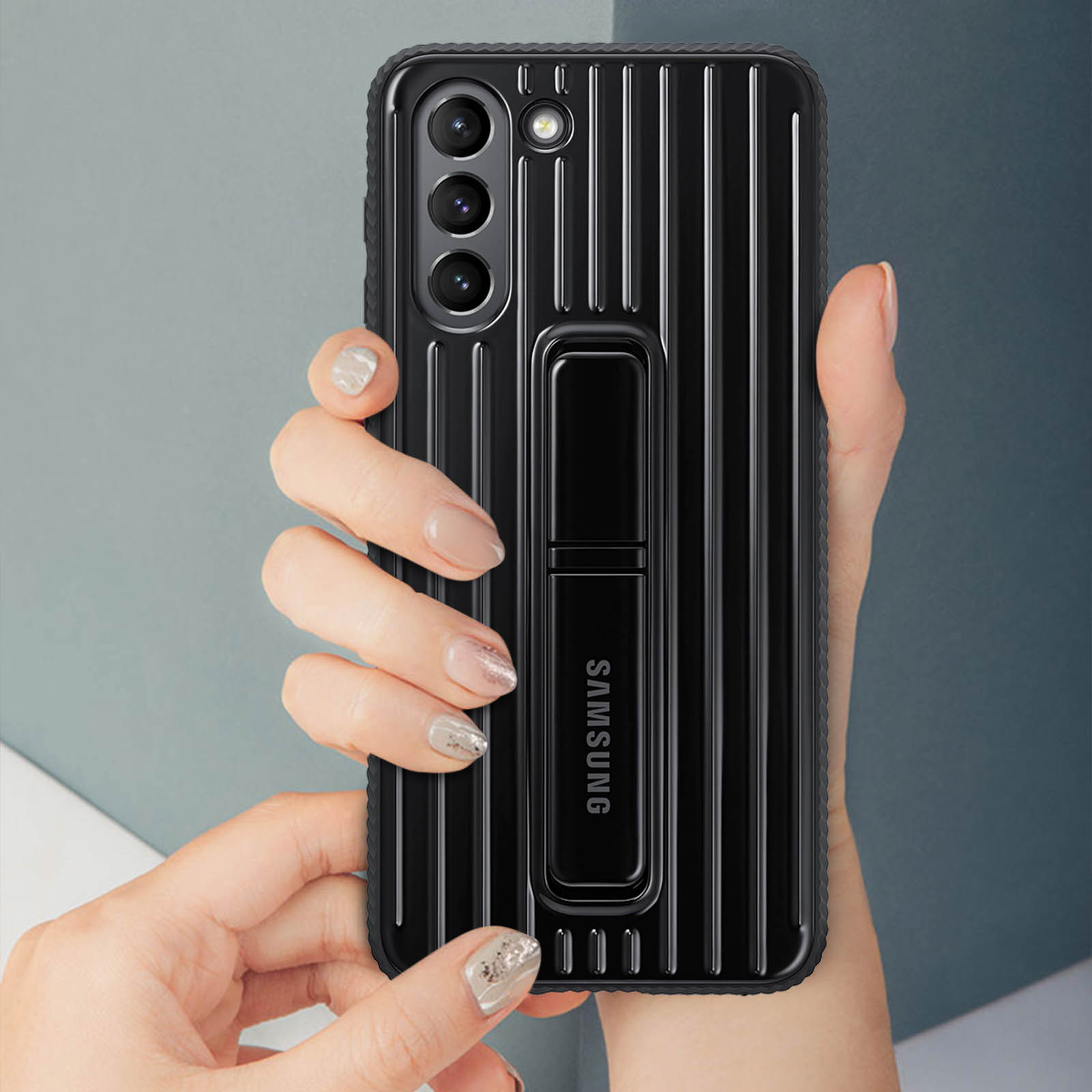 Funda negra con líneas verticales, sosteniendo un teléfono. Tiene un soporte y la palabra SAMSUNG.