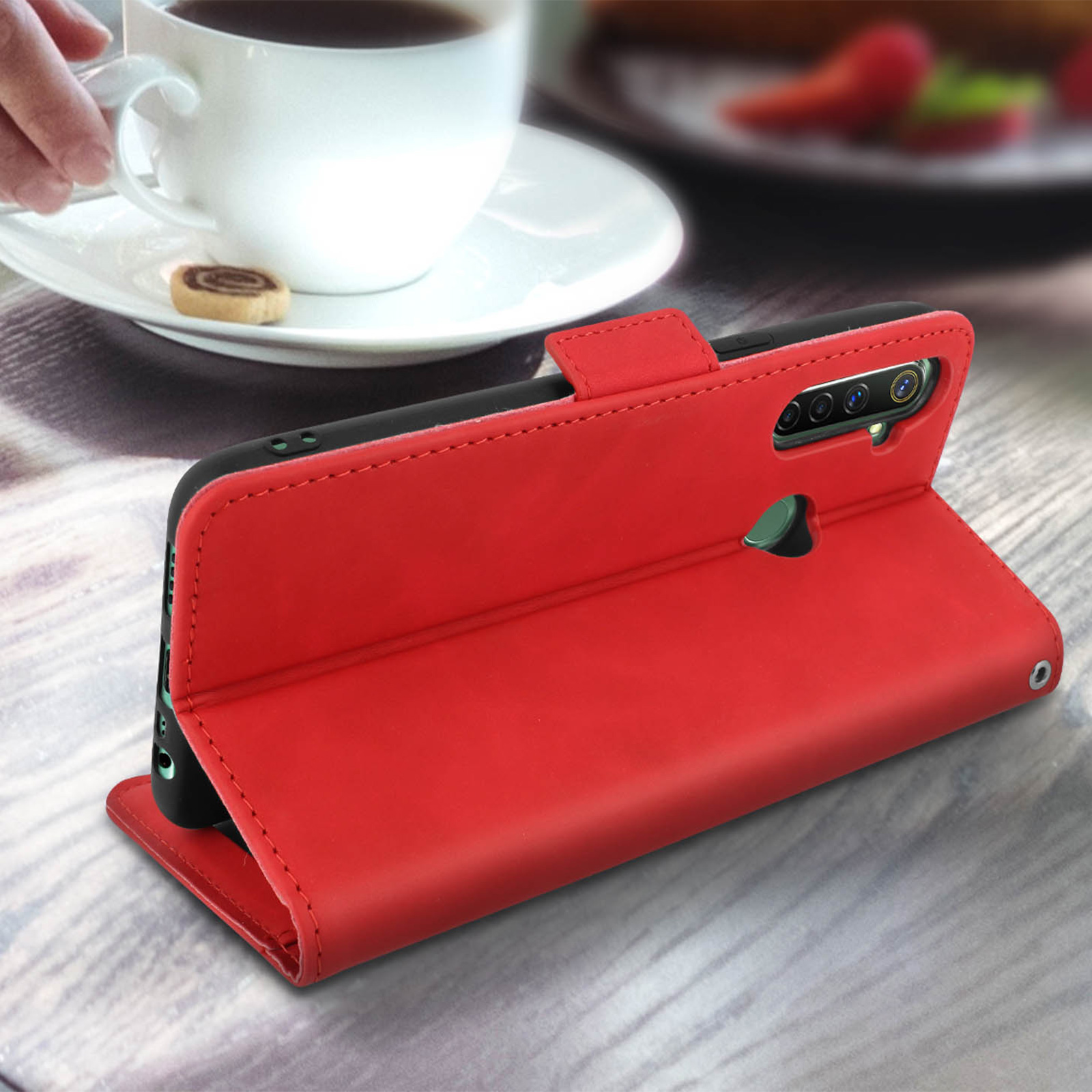 Custodia rossa per telefono in posizione verticale, con una tazza bianca e un biscotto sul tavolo.