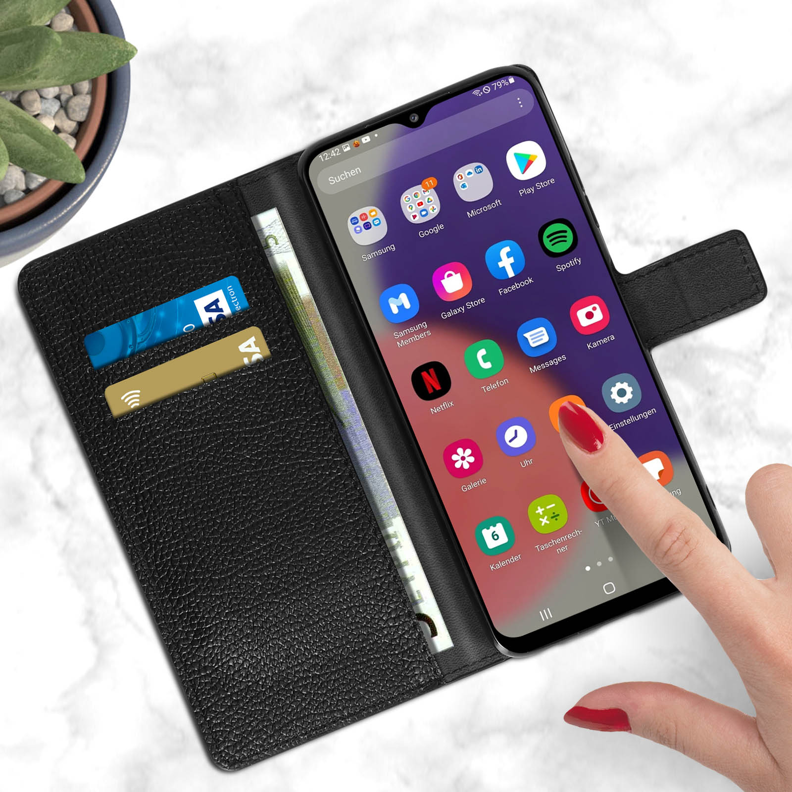 Ein Telefon in einer schwarzen Leder-Geldbörsenhülle wird gezeigt. Eine Hand zeigt auf den Bildschirm. Kreditkarten und Geld sind sichtbar.
