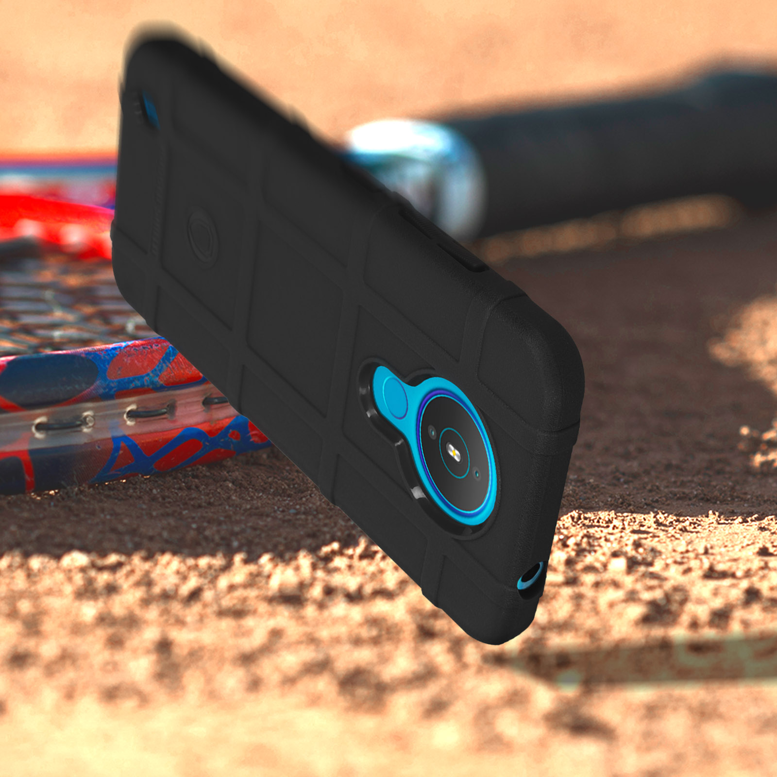 Custodia nera per telefono su superficie sabbiosa. Una racchetta da tennis sullo sfondo.