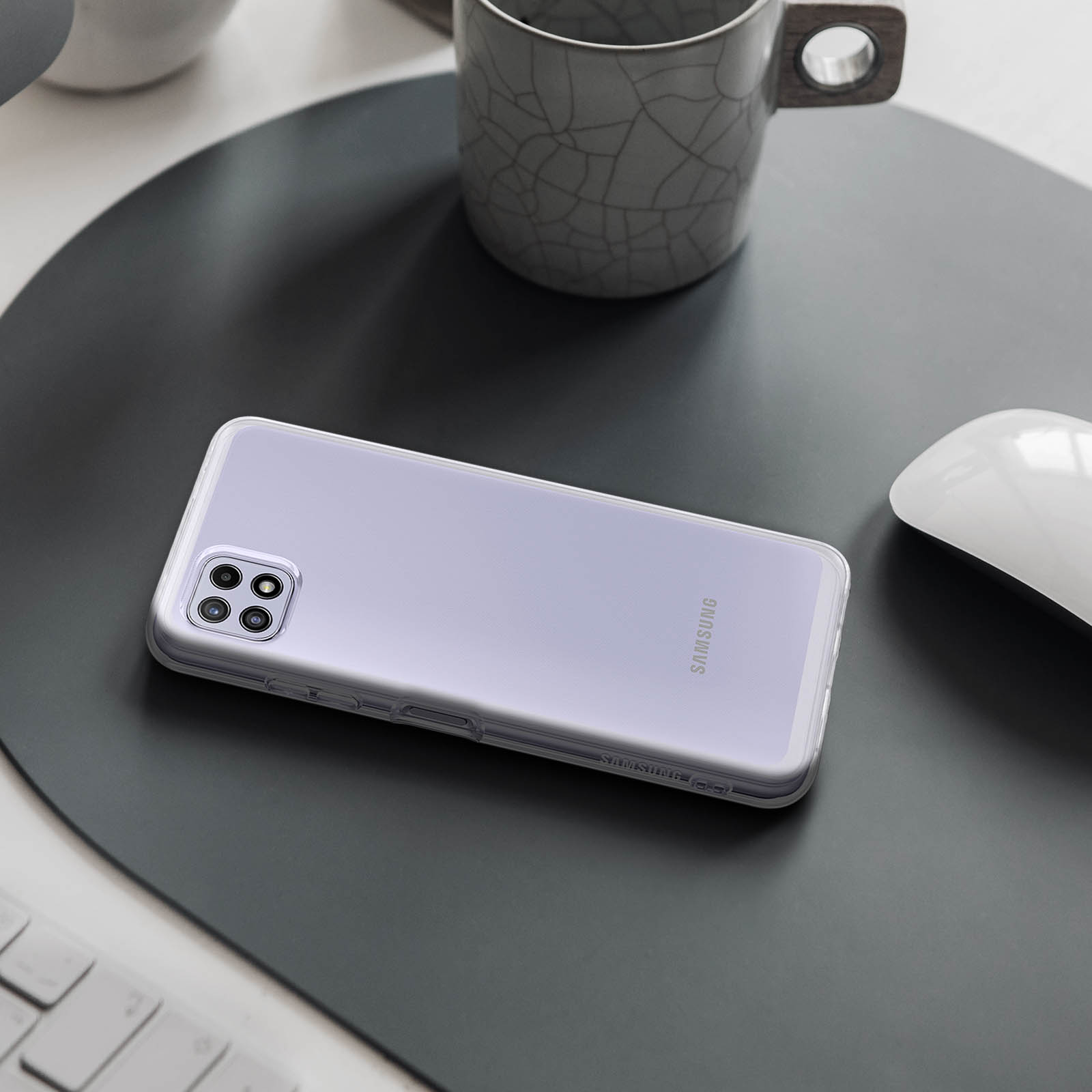Un teléfono en una funda transparente sobre una alfombra oscura, con ratón y teclado detrás.