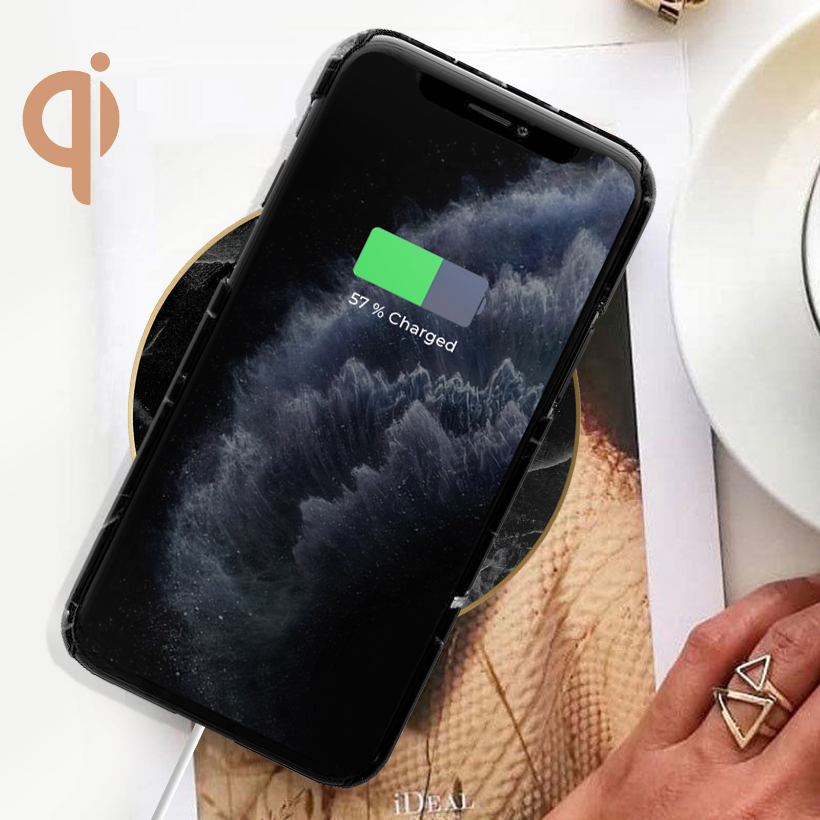 Telefono su un caricabatterie wireless, in carica. Il display mostra 57% caricato. Una mano con anelli.