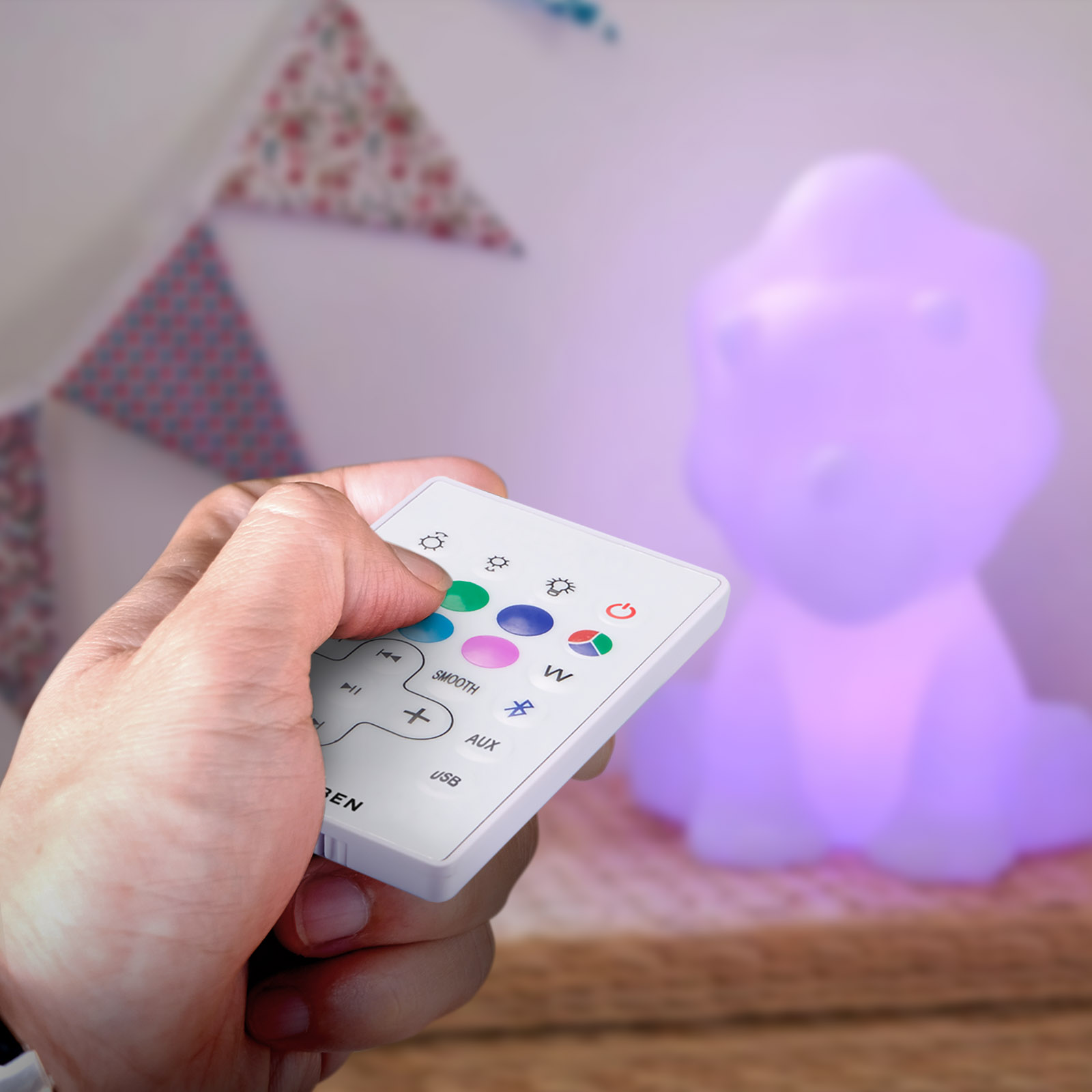 Ręka trzyma pilota skierowanego w stronę świecącej lampy w kształcie dinozaura.